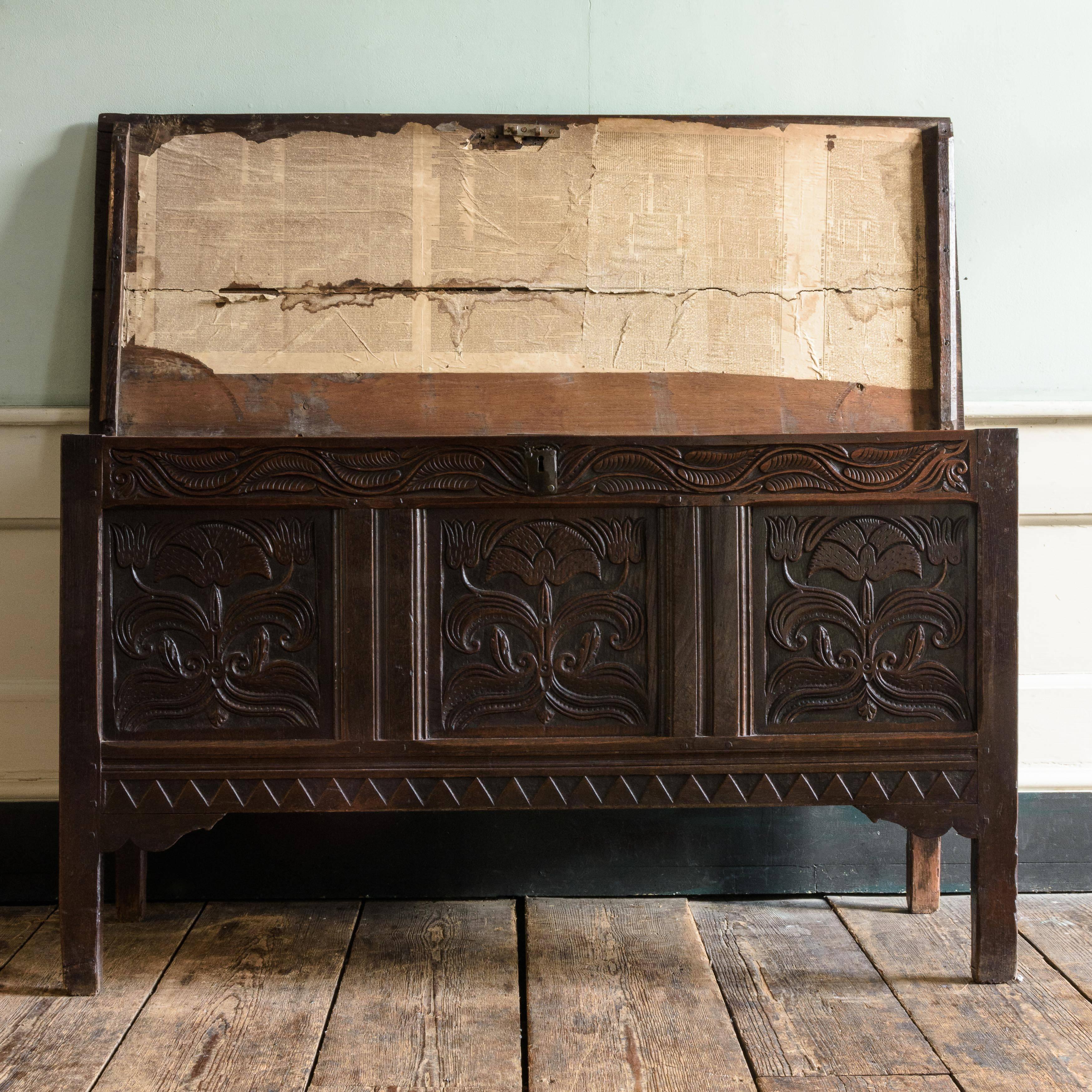 Charles II oak joined chest, with two board hinged top enclosing interior with candle box, the front with three panels carved with floral decoration, the frieze above with leaf carving, on stile feet.

Dimensions: 78 cm (30¾