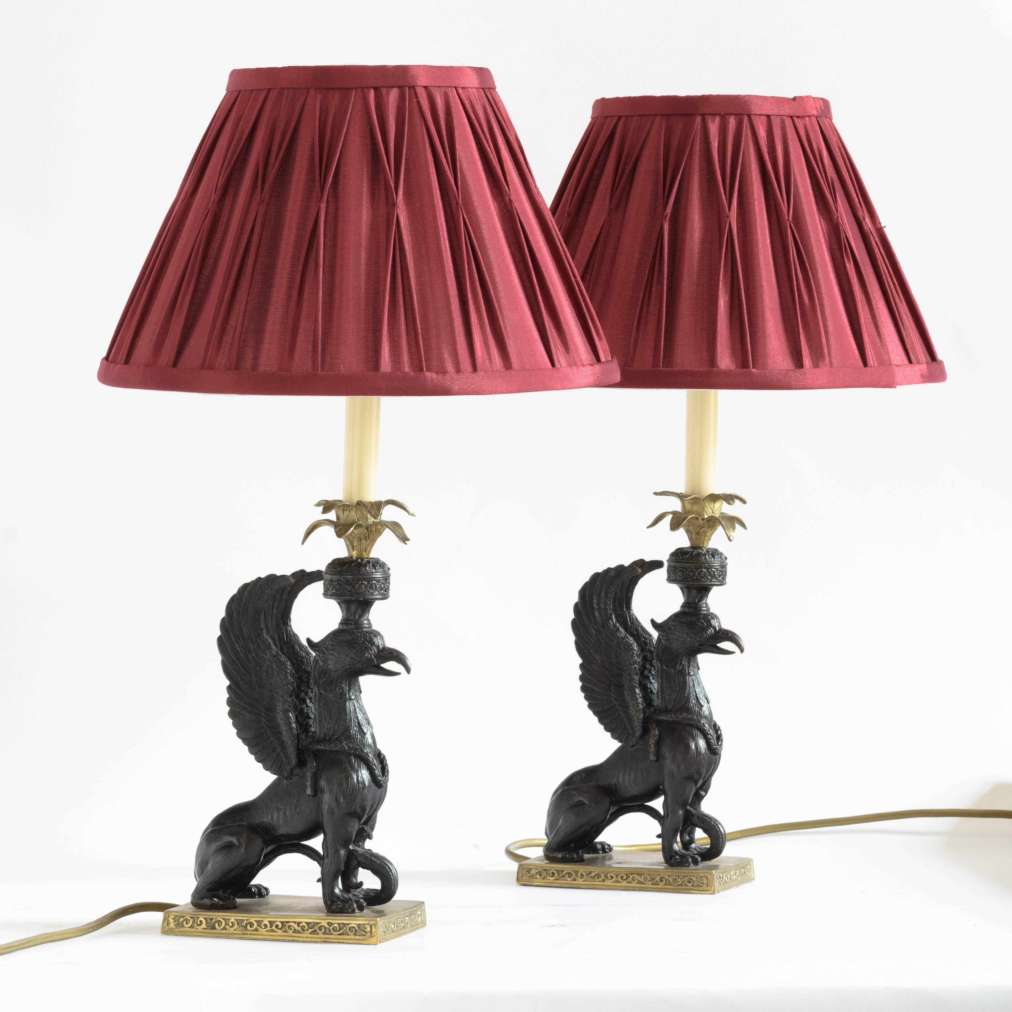 A pair of winged griffin bronze and brass table lamps, 20th century, after the 18th century originals by Sir William Chambers, with red shades.


The design of these griffin candlesticks is attributed to Sir William Chambers (1726 – 1797), court