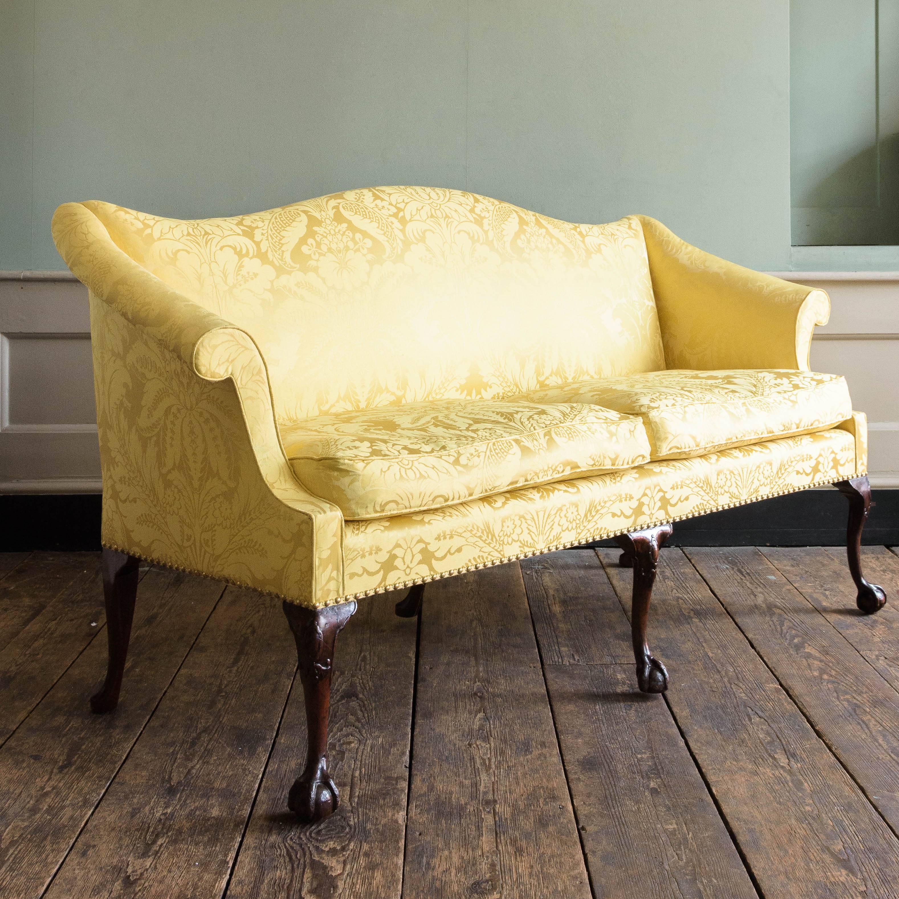 George II style mahogany humpback sofa, upholstered in yellow silk damask with squab cushions, on slender cabriole claw and ball feet. 20th century.