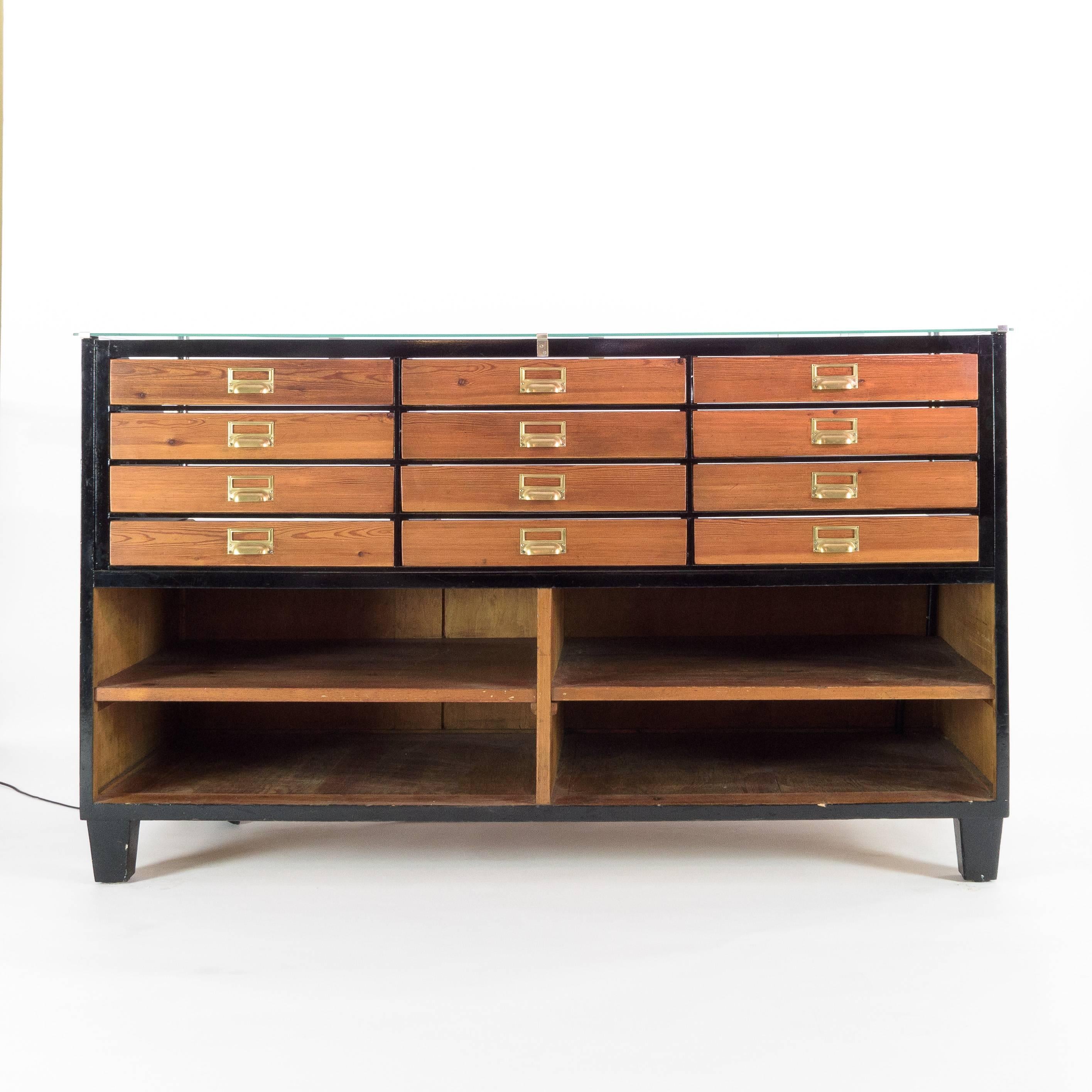 Mid-20th century ebonized haberdashery drawers, the arrangement of twelve graduated drawers above full depth storage, illuminated.