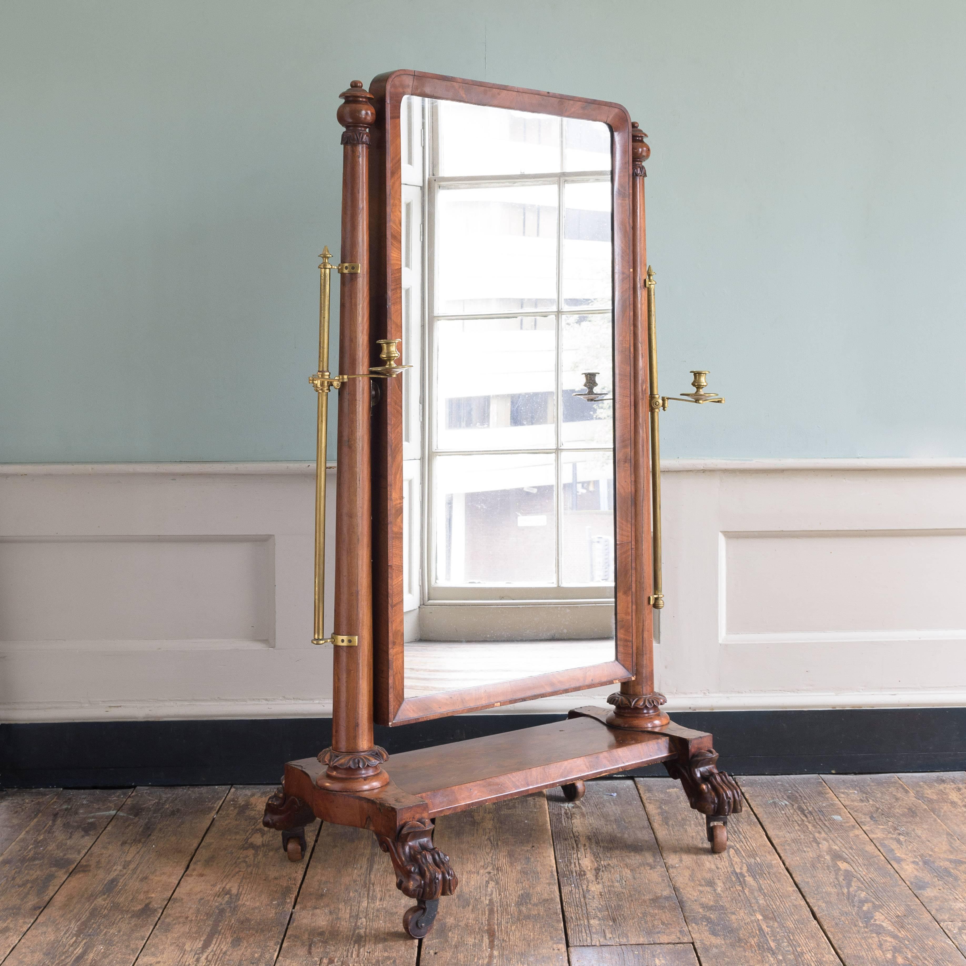 Mid-19th century mahogany cheval mirror, circa 1830-1840, the tapered cylindrical supports with adjustable brass candle sconces, on lion's paw feet with castors.