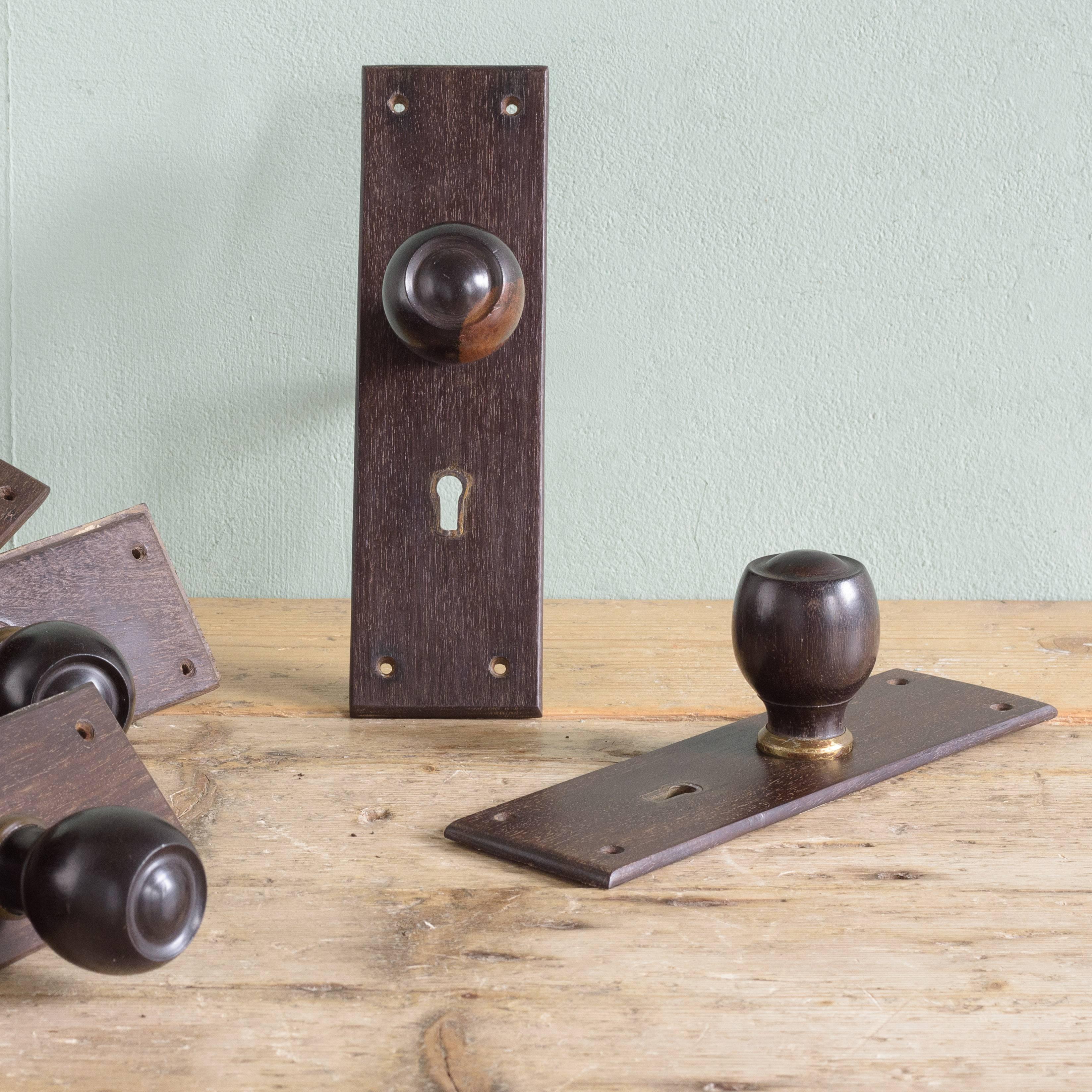 A run of eight pairs of 1920s turned ebony door handles, with brass collars on rectangular backplates.