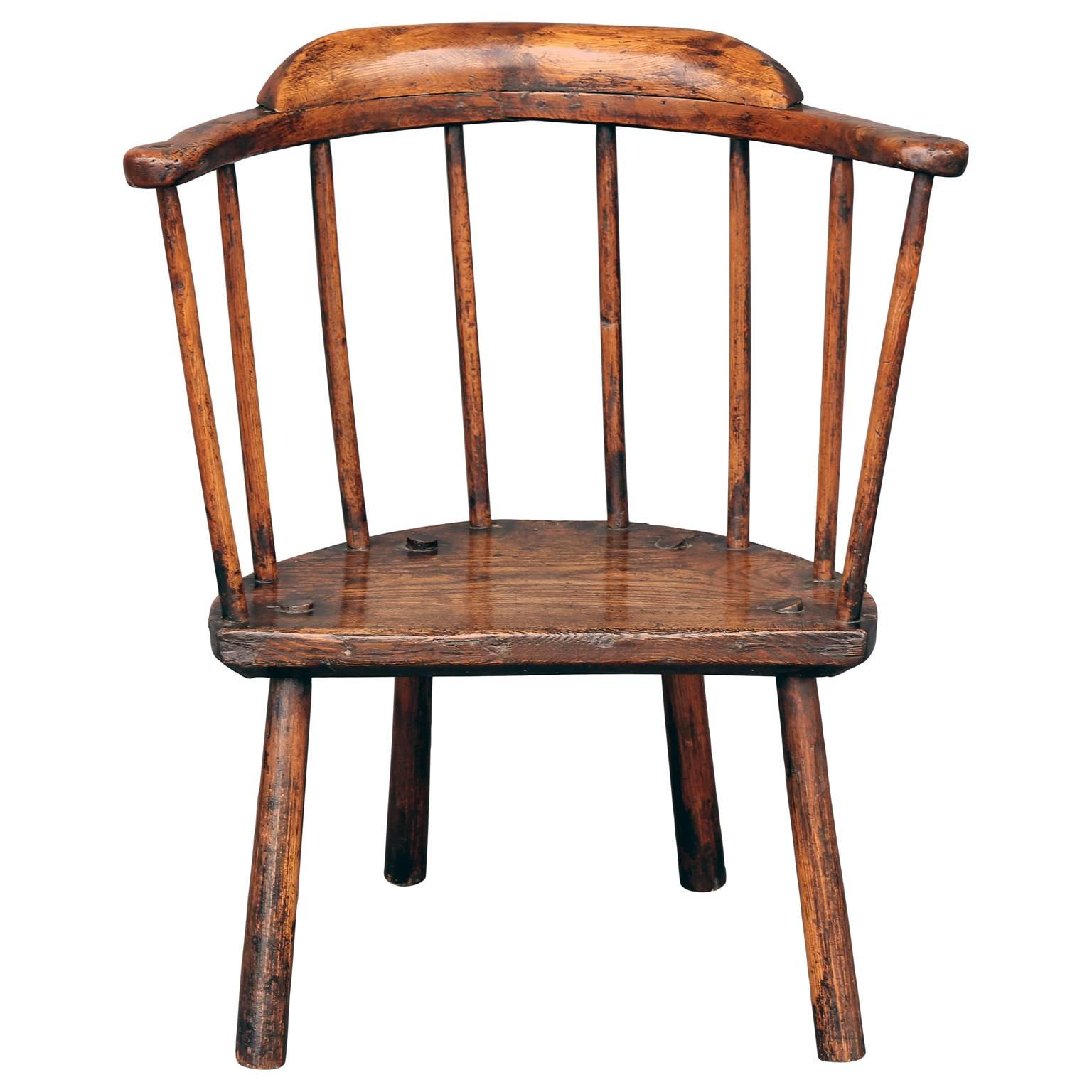 A wonderful, primitive early or mid-18th century Welsh stick chair from ash and oak wood with a well-patinated finish and morticed construction. Its one-piece horse-shoe shaped arm, four legs and upright spindles are ash; and its thick plank seat is