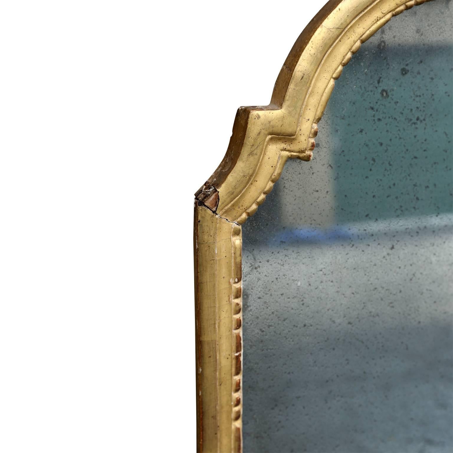 Petite arched-top mirror (18th century French). Carved gildwood frame containing original - or very old - mirror. Mirror features a liberal amount of subtle, attractive spotting from age.