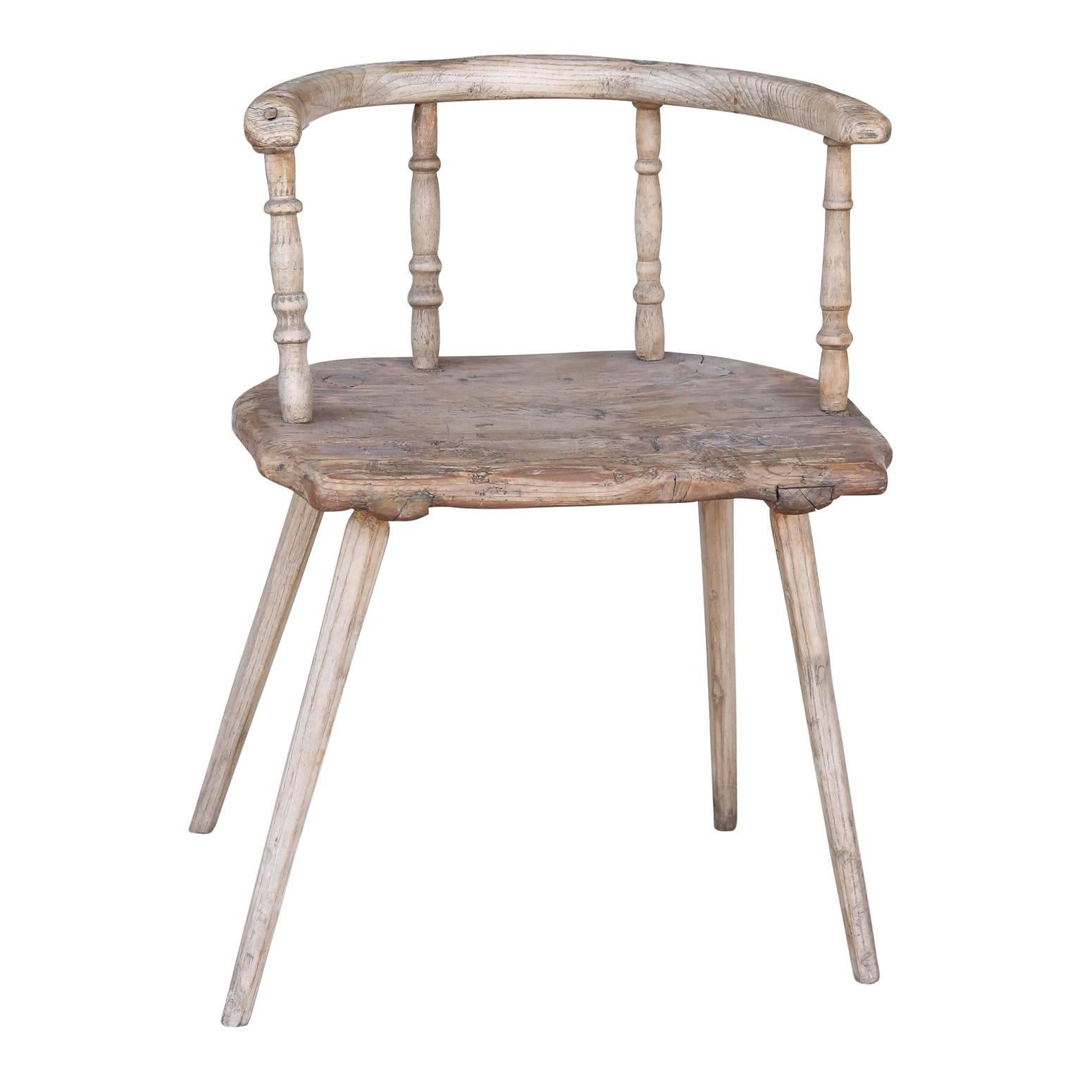 19th century Swedish elmwood chair in a pale dry finish with horseshoe back rail supported by turned spindles pegged into a thick plank seat on four carved legs.