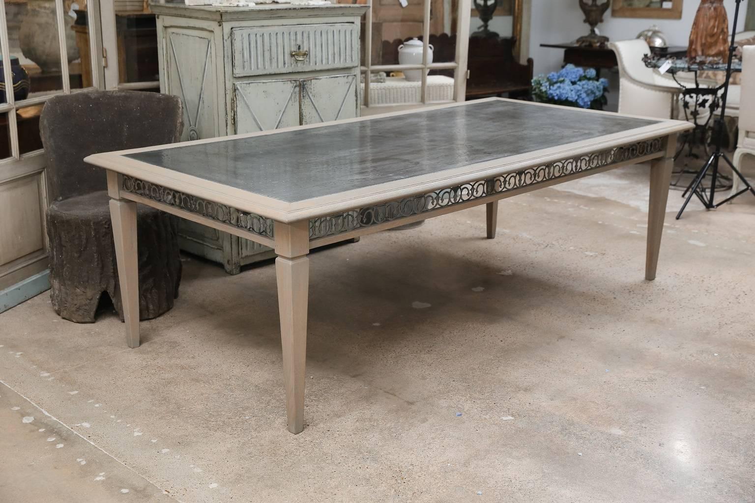 Custom carved dining table from French white oak with four tapered legs, a zinc-alloy top and a decorative metal apron reticulated in a scrolled motif. The oak surfaces and metal apron both are finished with a subtle semi-transparent gray wash.