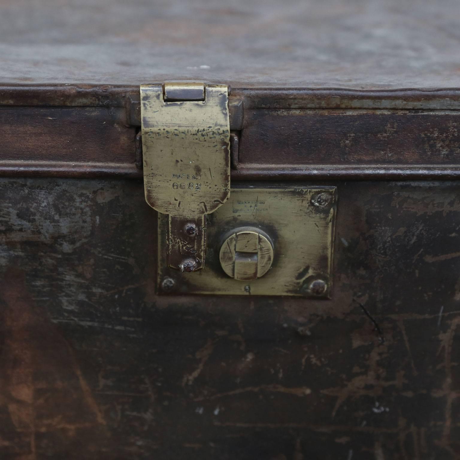 Early 20th century metal trunk set in carved plinth base. The trunk boasts a rich, mottled patina reflecting years of natural wear, while the later carved plinth base is decorated with faint remnants of aged white paint. The interior of the trunk is
