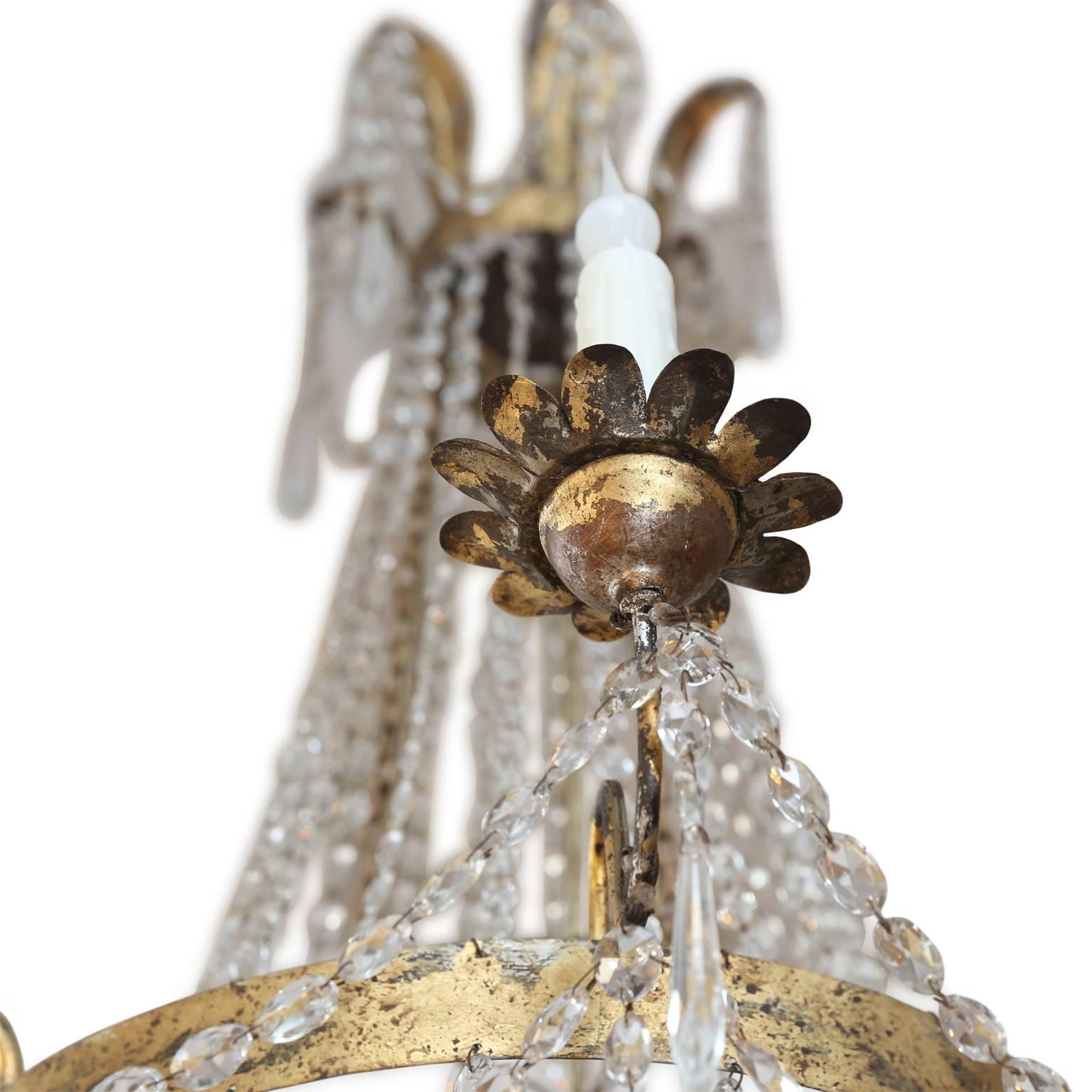 An elegant chandelier in the Neoclassical style from Milan dating to the late 19th century comprised of three metal tiers gilded in silver and gold connected by crystal chains and garlands. The upper crown-like tier is decorated with tole leaves and