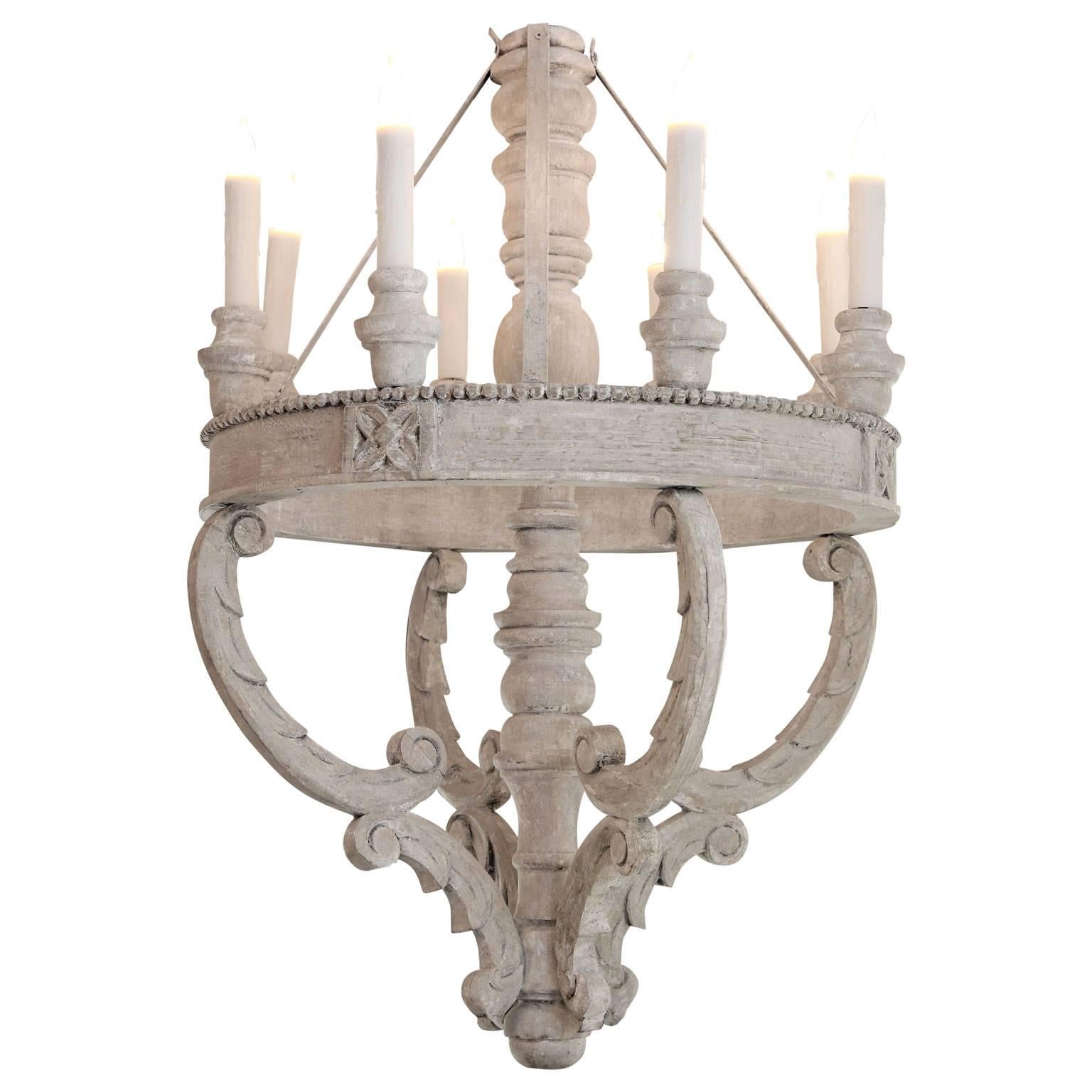 Large painted wooden chandeliers: eight-lights arranged around a 33 inch diameter ring with a carved beaded edge, supported by four sets of opposing C-scrolls and a central turned-body. Traces of gold leaf are visible from wear to the gray-white