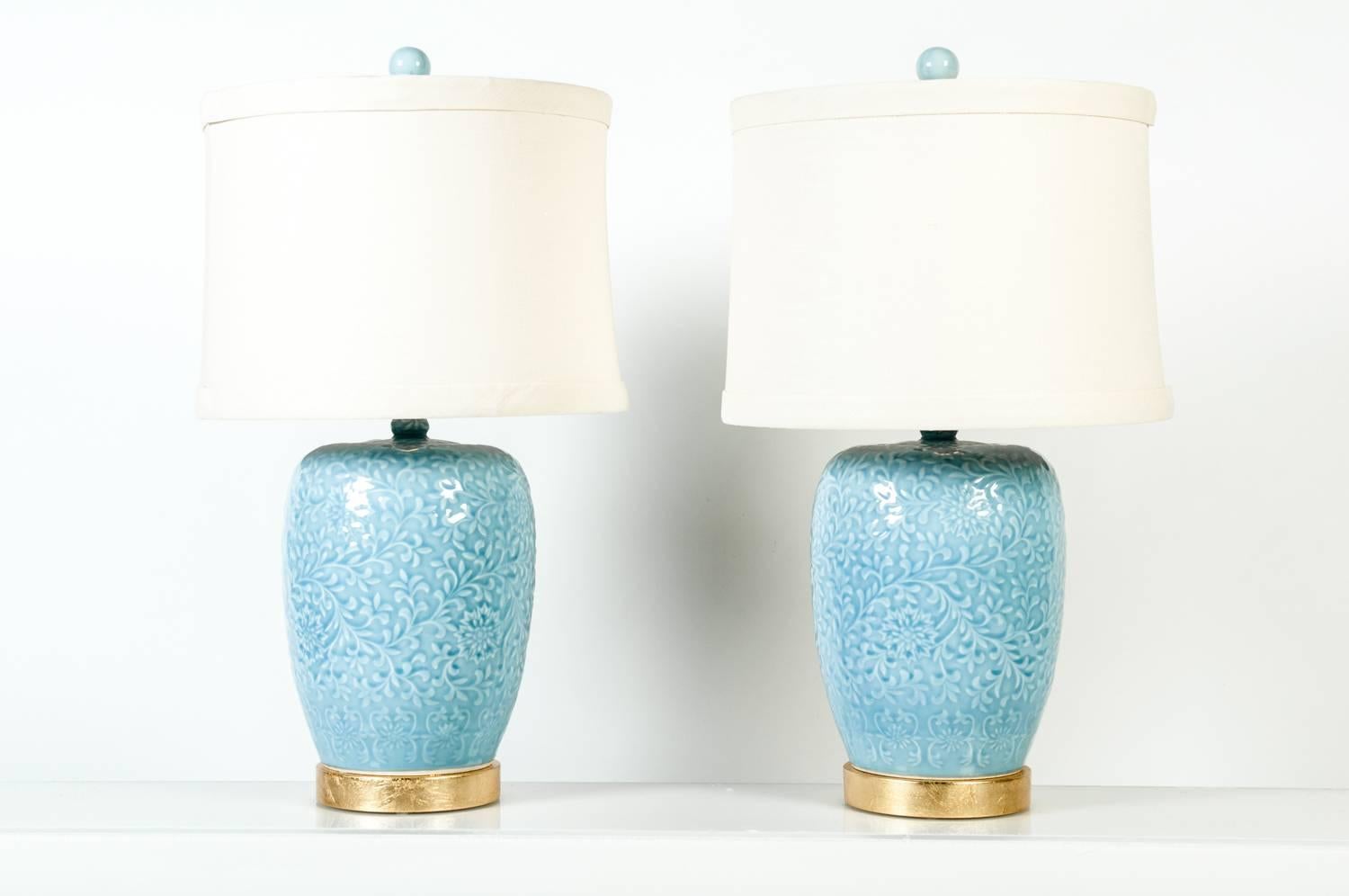 Pair of powdered blue porcelain task / table lamps with subtle vine and floral design underglaze with gilt brass base , and matching finials. Each lamp sit on a wooden gilt base. Each lamp measure 26.5 inches tall with finial x 8.5 inches wide in