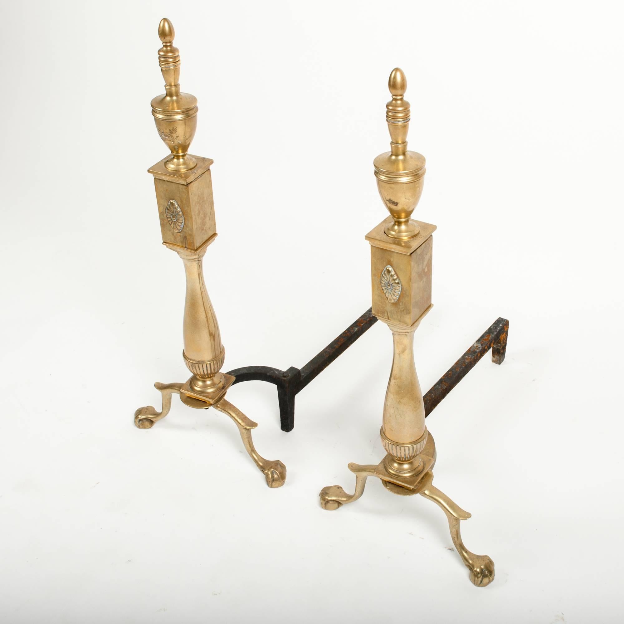 These brass andirons have claw and ball feel, as well as urn and spindle finials, and squared accent to body.