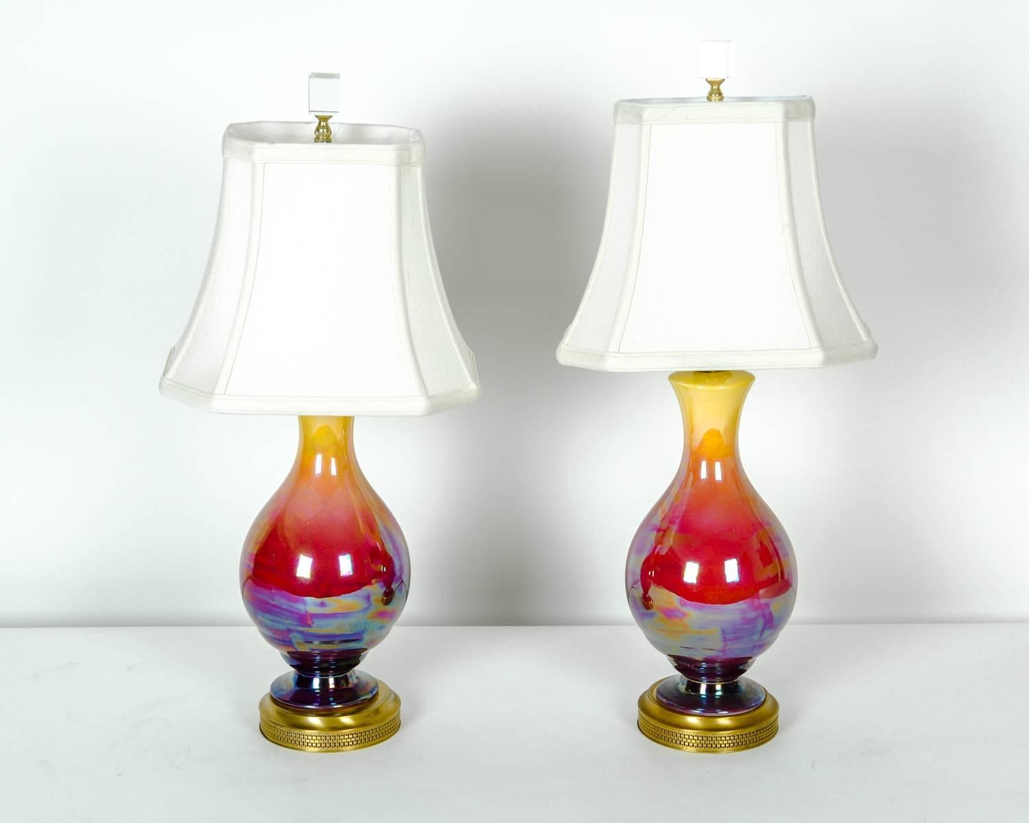 Vintage pair of iridescent porcelain table lamps with brass base. In excellent working condition. Each lamp comes with a linen shade. Each shade measure 8.5 inches long x 10.5 inches base. Each lamps measure 21 high x 6 inches diameter.