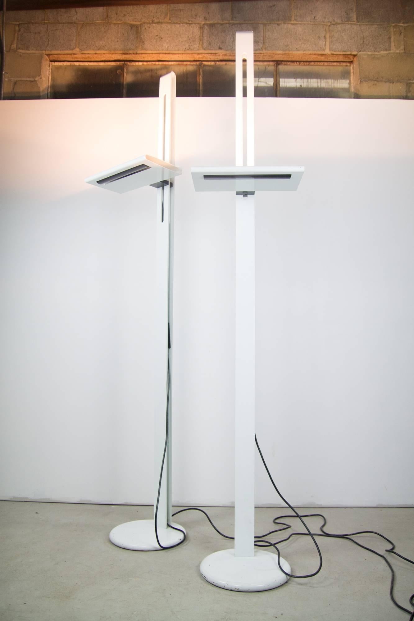 A pair of towering Postmodern Italian floor lamps in steel. The lamp heads adjust up and down the top third of the rail and articulate left and right. The halogen light is dimmable via switches which can be concealed within the lamp body. Shade