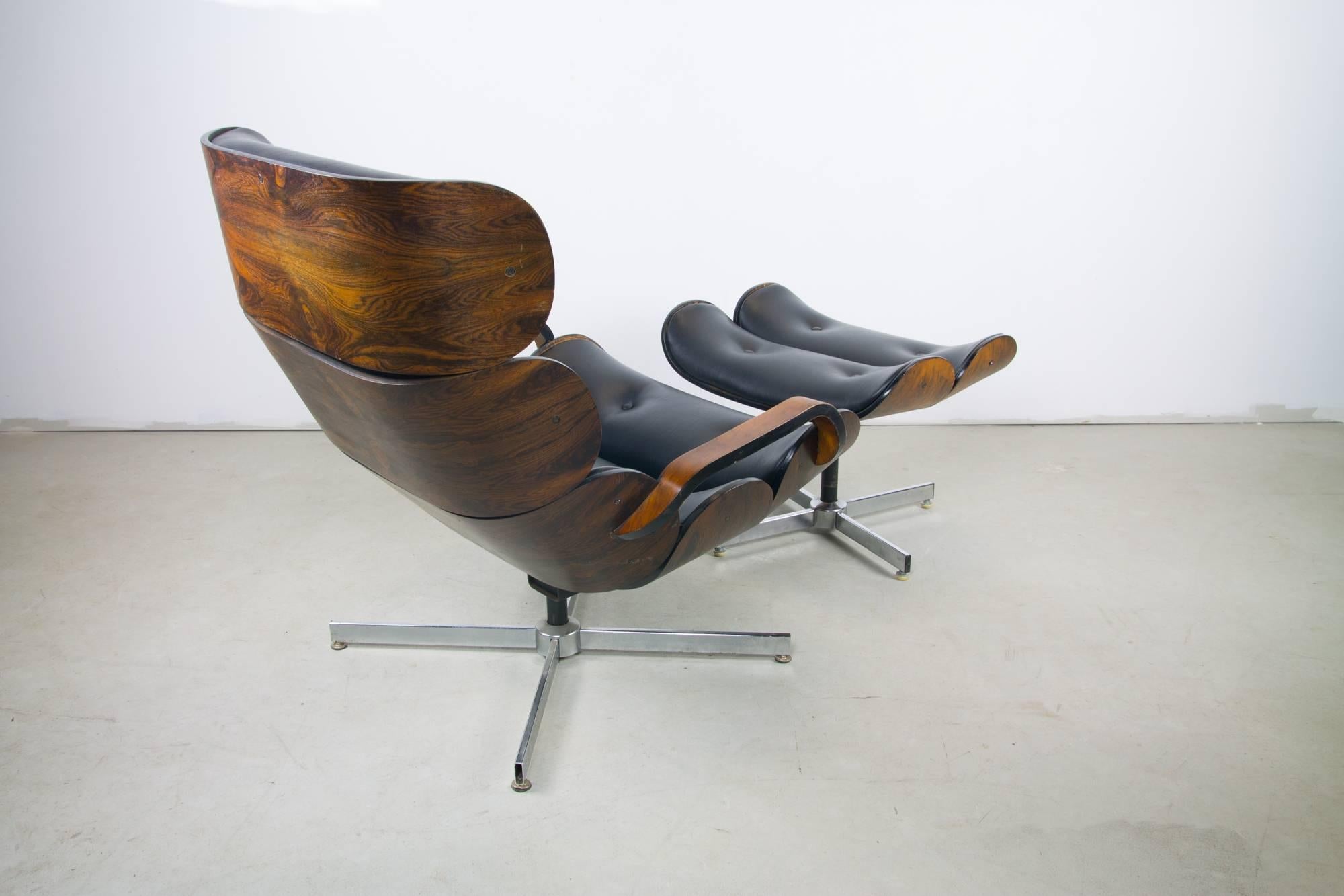 Stunning clamshell lounge chair and footstool by George Mullhause for Plycraft featuring buttoned Naugahyde engulfed by figural rosewood veneer. The chair swivels and tilts. 

Footstool measures: 16