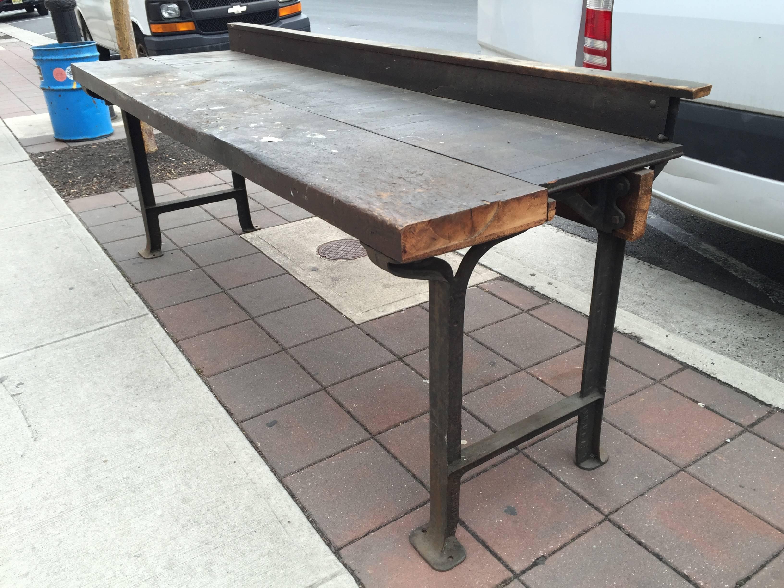 Perfectly patinated and distressed long Industrial factory work bench with a wood top and back rail, set atop elegantly formed iron legs and frame.