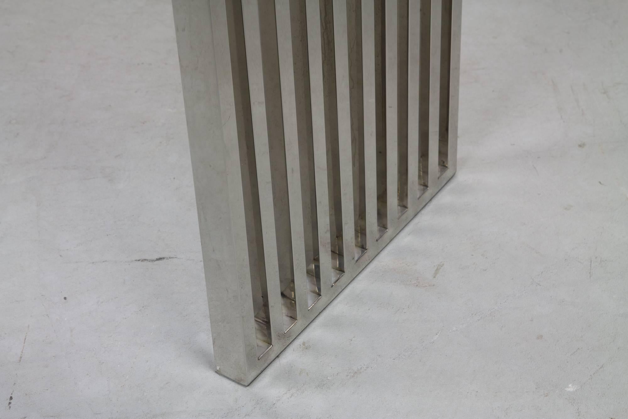 Linear monolithic waterfall console with continuous chrome slats and thick glass top.