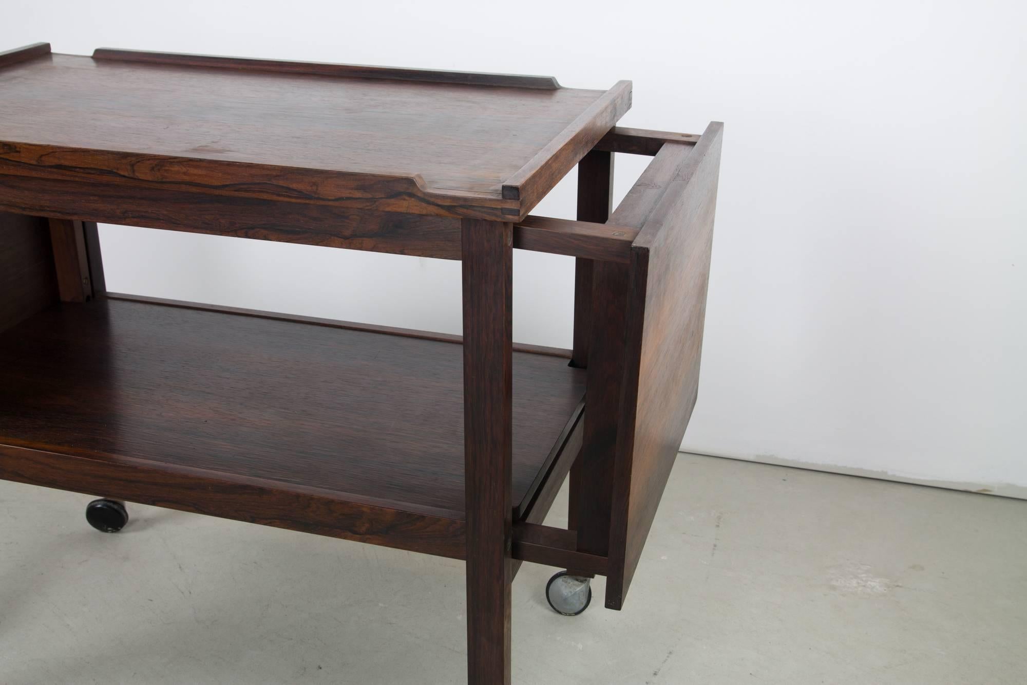A cunning convertible rosewood bar cart with concealed side tables which tuck into either end. The cart features solid rosewood construction and hand-cut joinery and is set atop smooth orbit casters.