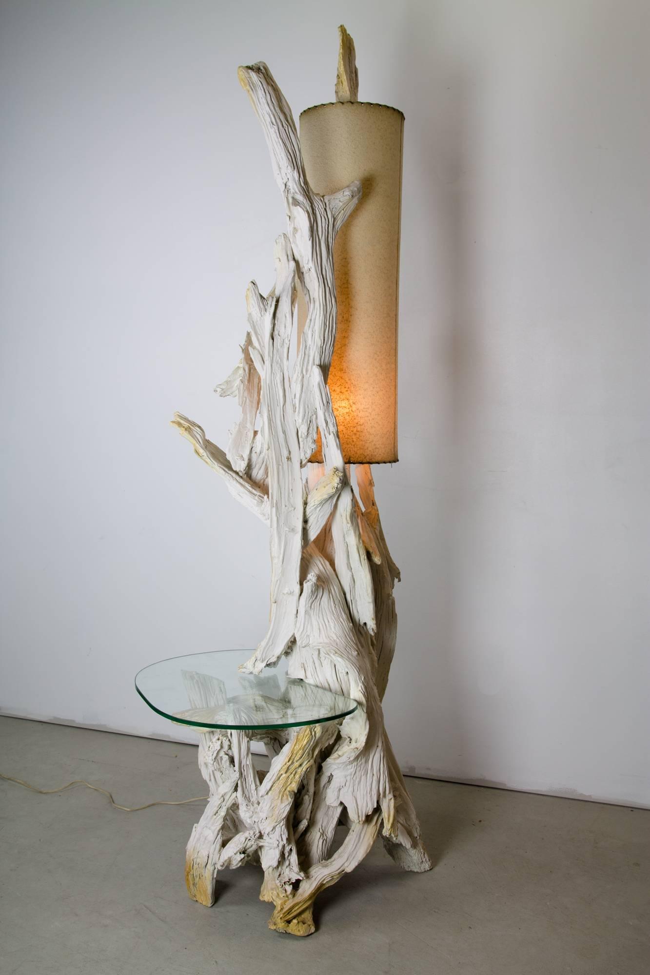 A large-scale free-form driftwood floor lamp with removable floating glass table, tall cylindrical fiberglass lampshade, and discreet driftwood finial.