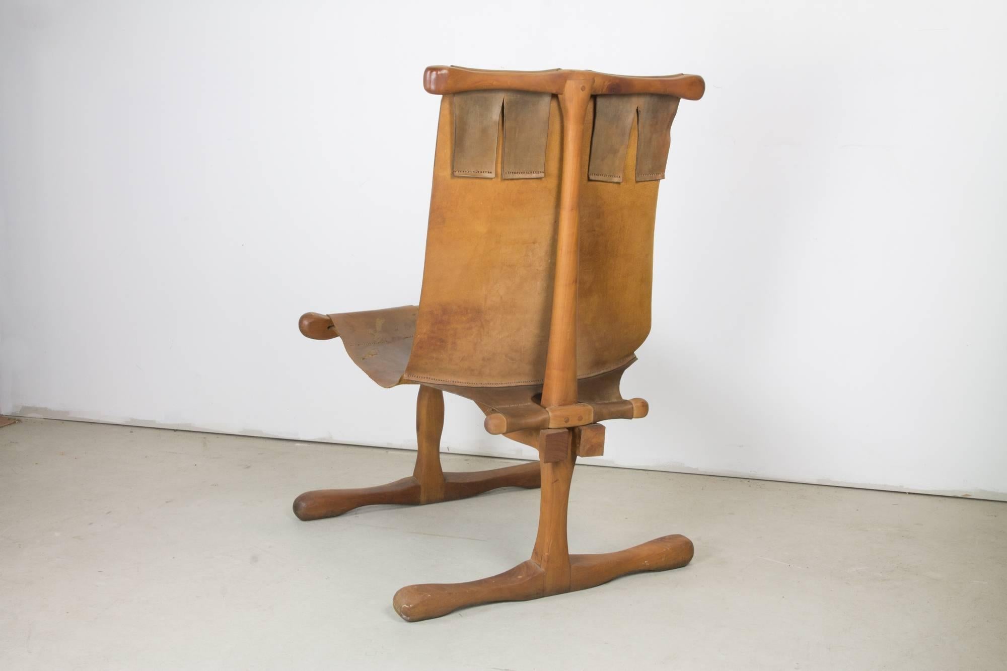 Rare American Studio Craft movement carved and pegged wood frame chair with sled base and robust t-frame construction supporting a broad saddle leather sling. Optional worn hide leather pillow is hung from back with leather strip cord.