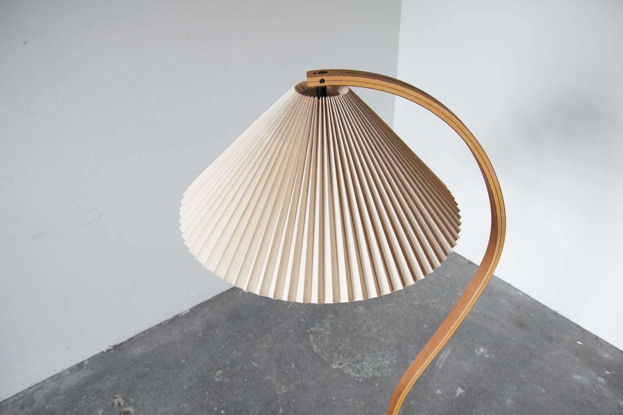 Bentwood floor lamp by Caprani Light AS, with original pleated shade. In it's snaking ascent, the laminated birch frame encompasses the angular shade. On a crescent shaped base of cast iron.