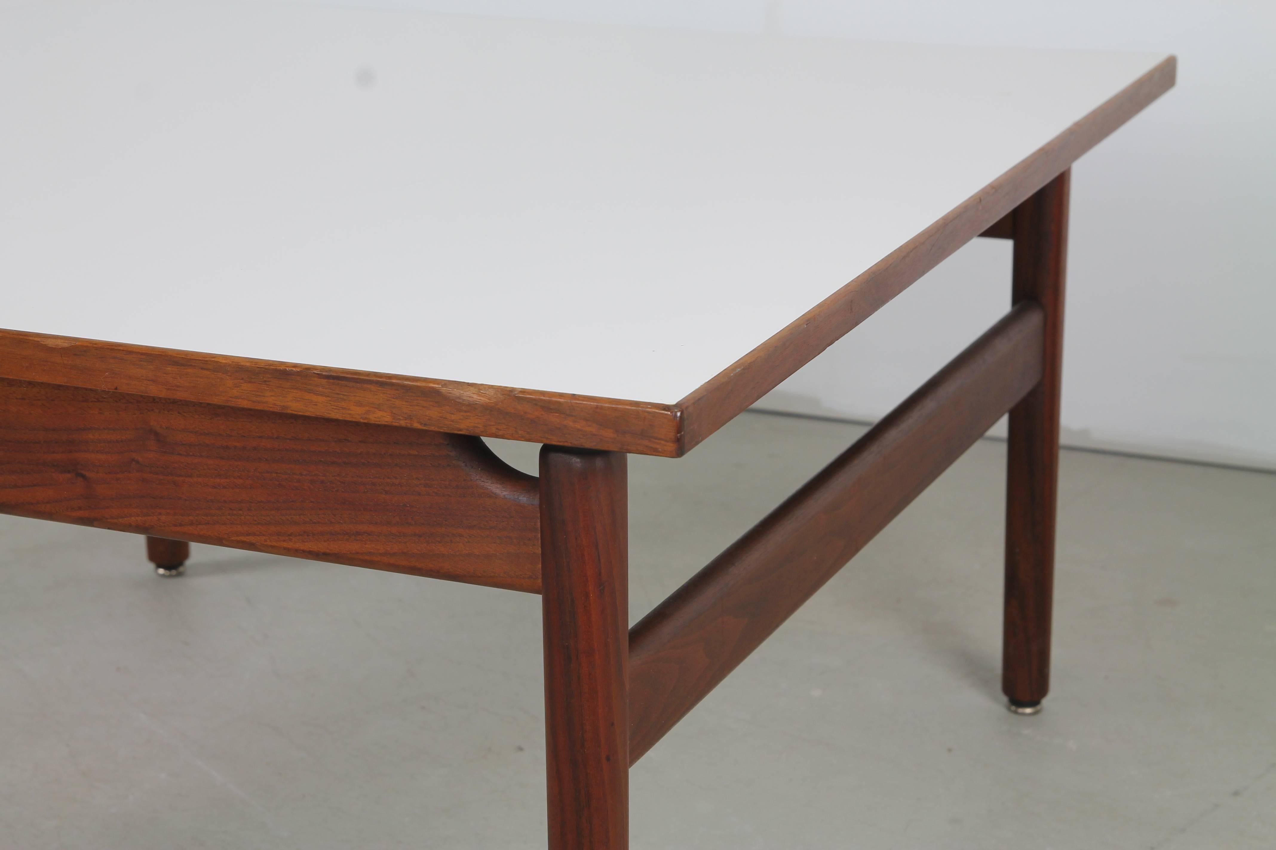 Versatile square coffee or cocktail table by Jens Risom, with straight, turned walnut legs, squared stretchers and a floating white laminate top.