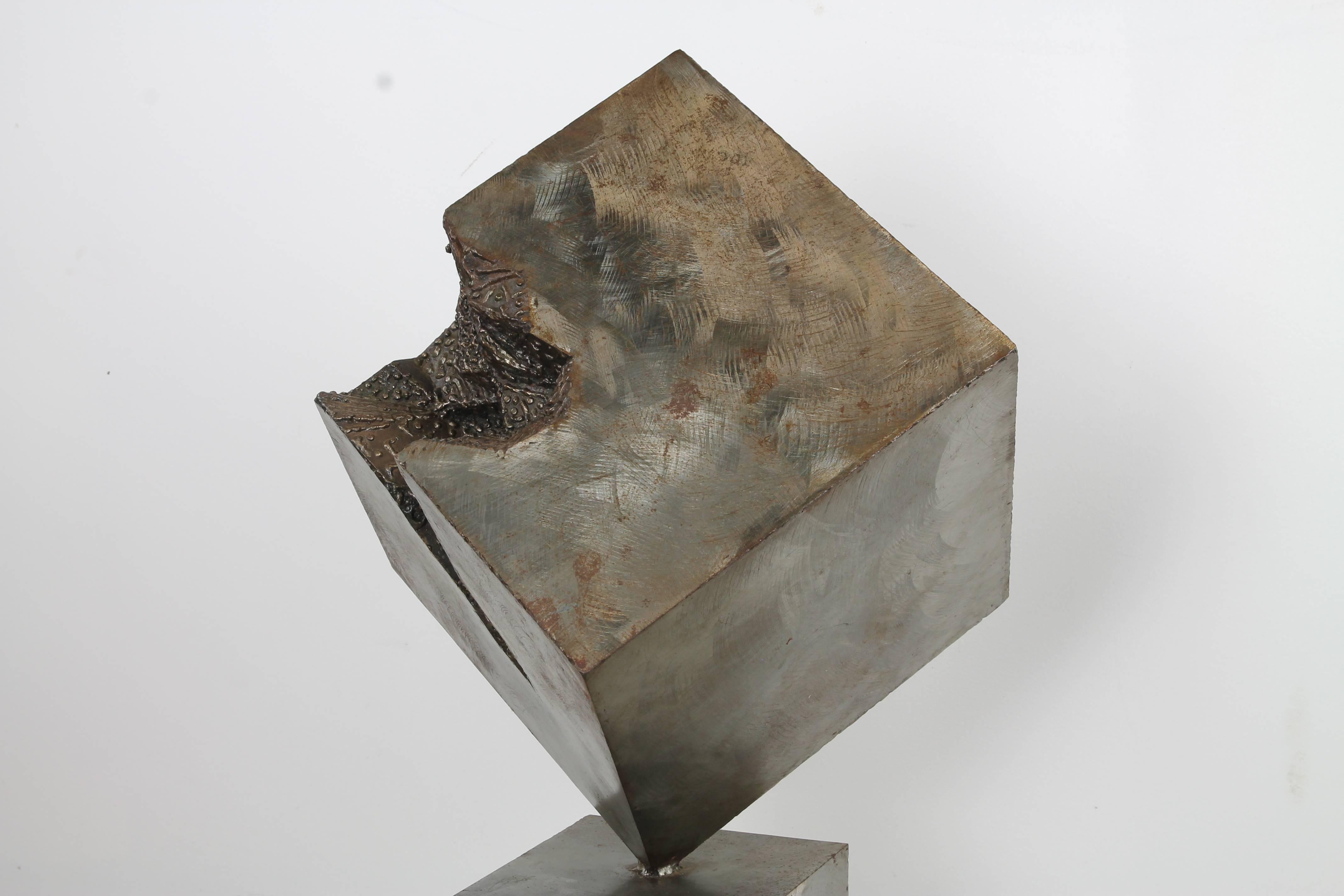 A monolith sculpture in Brutalist tradition, comprised of a skewed steel cube with crater hole in corner, atop a rectangular steel pedestal. Signed 'Ladd' at base.