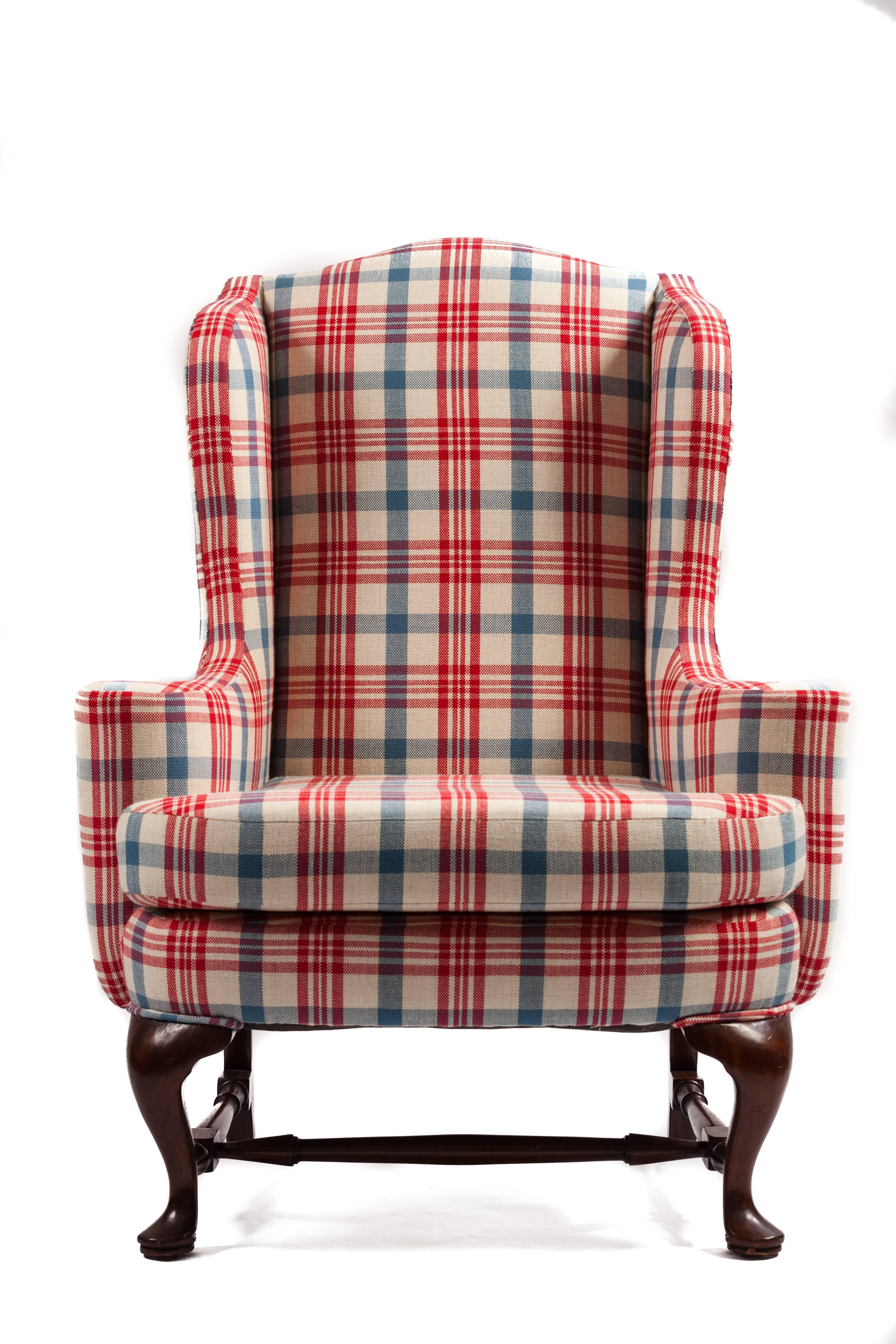 Queen Anne style upholstered wing chair. Serpentine crest rail, winged back forming scrolled arms, upholstered over frame with loose seat cushion, cabriole legs connected by round turned stretchers. Newly upholstered in custom plaid.