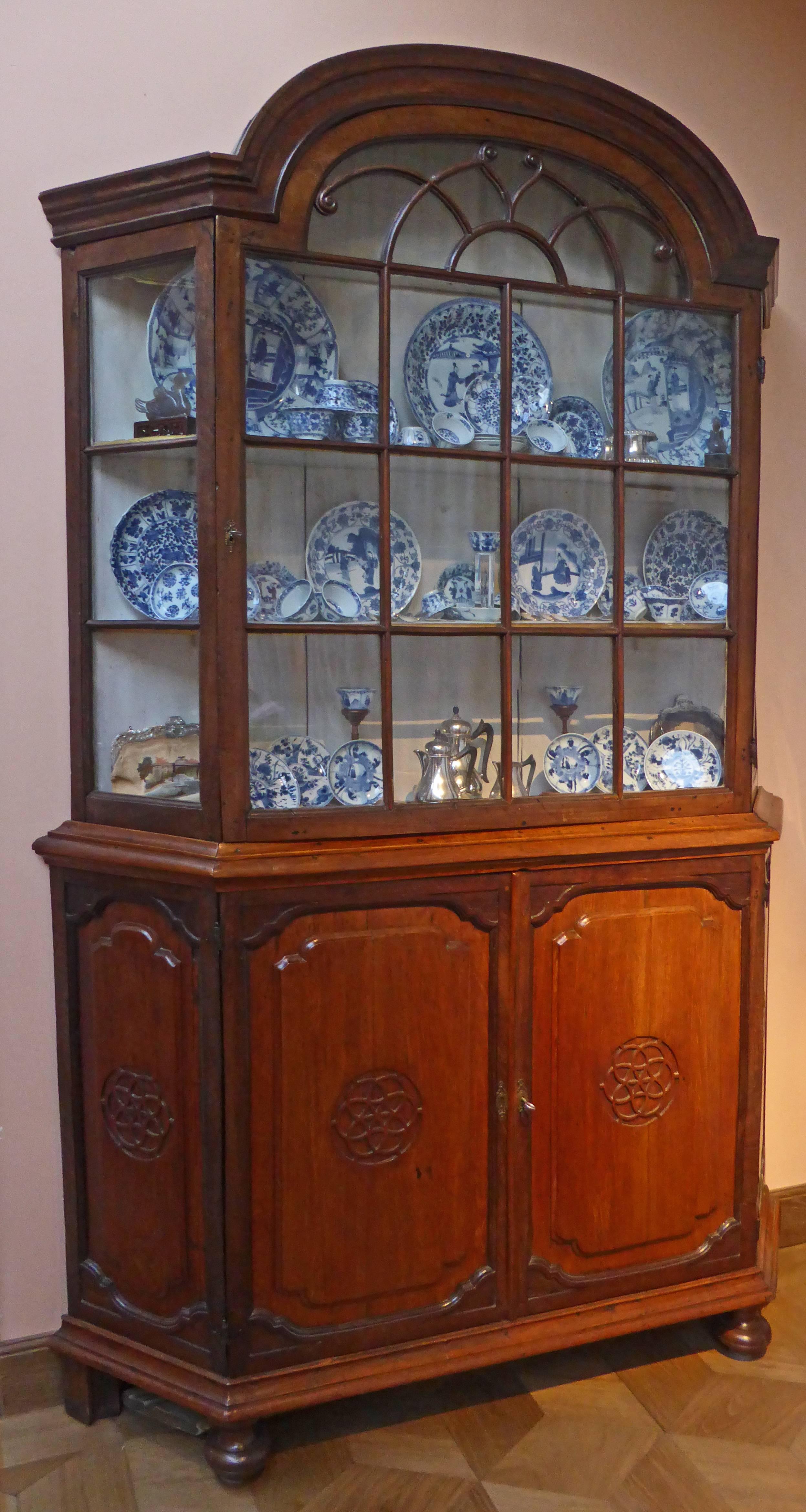 An early example of a display cabinet made of massif exotic woods with original pins and hinges.The arched cornice, one glazed panelled door, enclosing a plain interior with three shelves, glazed panelled corners, the lower part with two panelled
