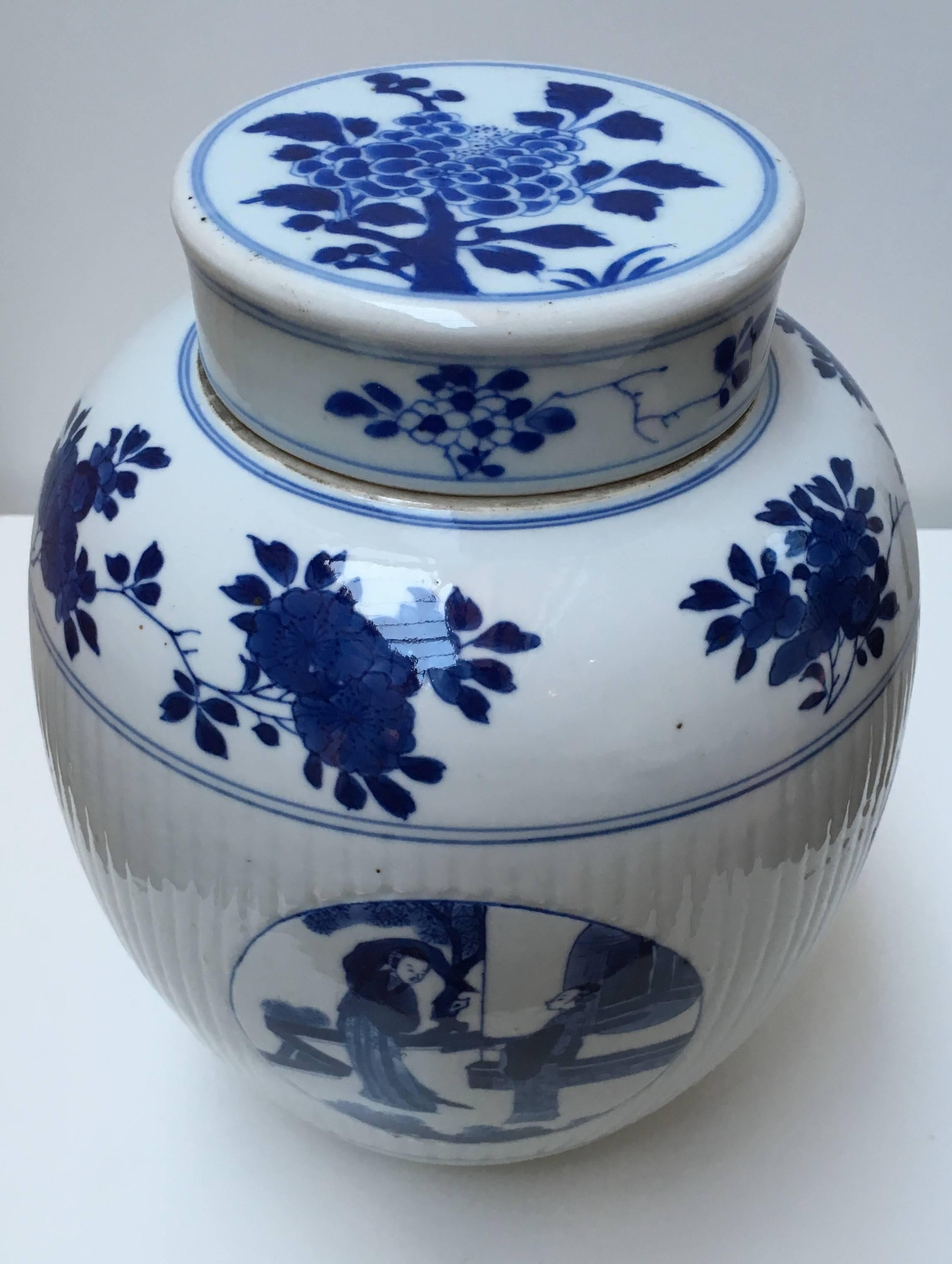 Ovoid, with ribbed middle section, the wide cylindrical cover over a short unglazed neck, decorated in underglaze blue with four medallions with scenes of two Chinese ladies. The top and cover are decorated with floral motifs, the bottom with a band