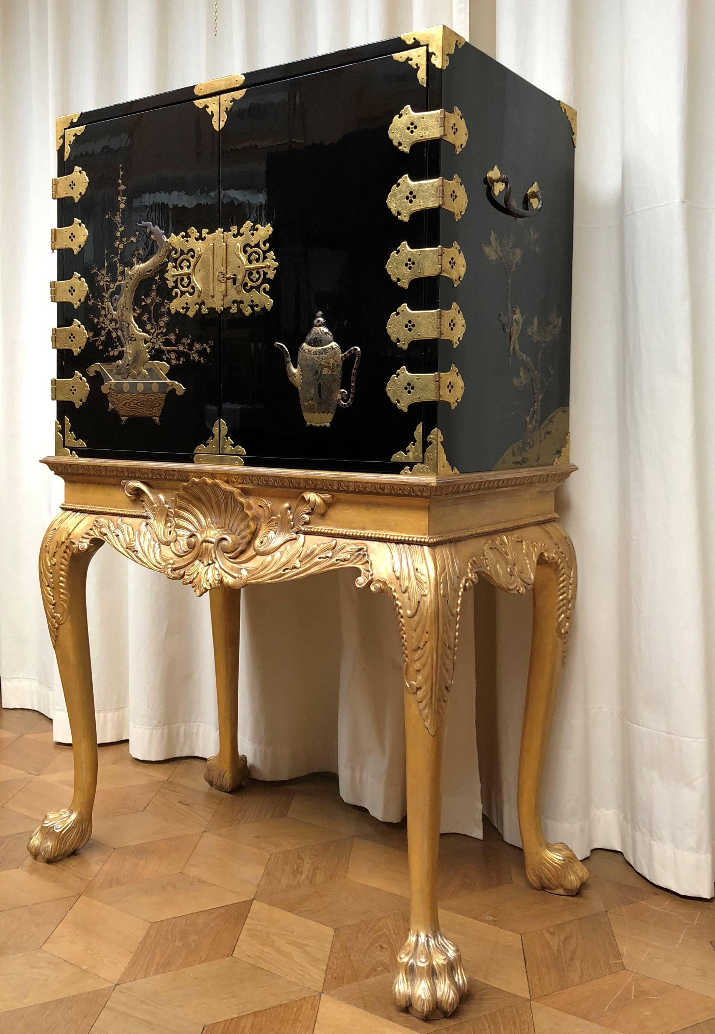 This rectangular lacquer cabinet is executed in black and gold reliëf lacquer. The hinged doors decorated with a teapot and a bonsai tree, opening to an interior fitted with ten drawers decorated with landscapes, the sides each with two birds on a