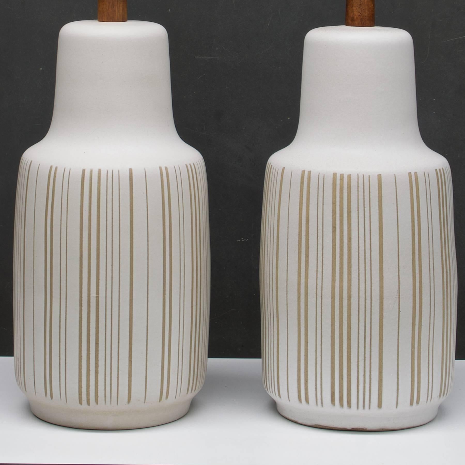 Matte glaze lamps bodies with incised variable width vertical stripes. Both with original finials.