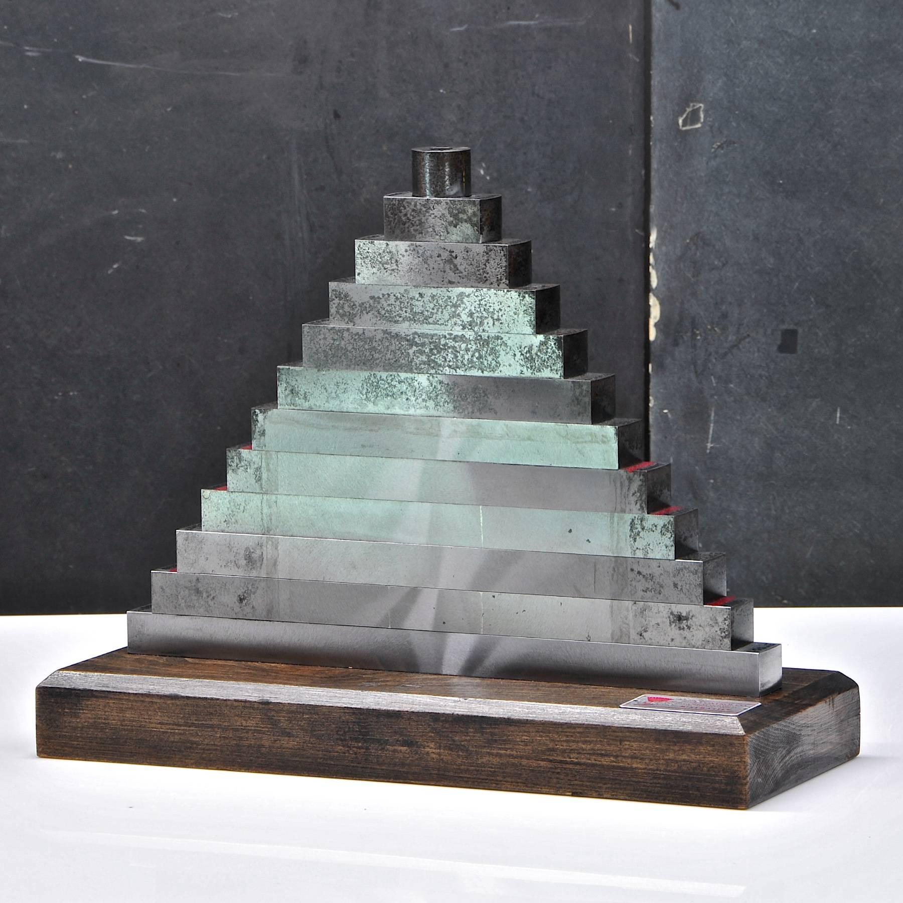Sculpture pyramidale de machinistes empilant des appareils de mesure en acier massif. Quelques taches d'oxydation sur l'acier, pas de bosses ni de dommages dus aux chocs. Sur un socle en bois noir. Très lourd.

Mesures : L 13¼ x D 5 x H 10½ po.