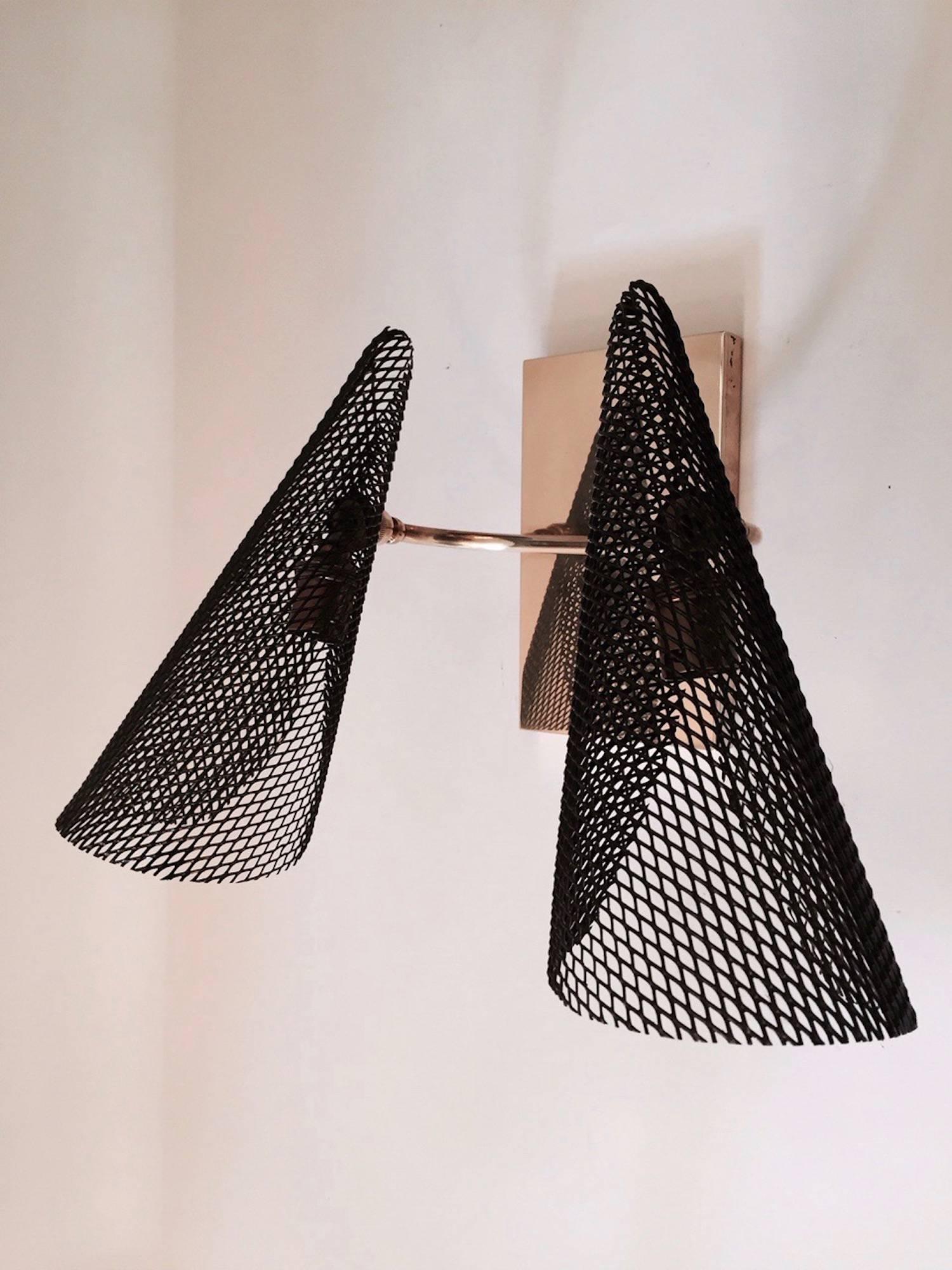 Pair of 1950s sconces attributed to Jacques Biny.
Composed of a rectangular brass plate decorated with a gilt brass arm.
On each end of the arm, a black perforated sheet steel cone is mounted on a swivel joint.
Two bulbs per sconce.