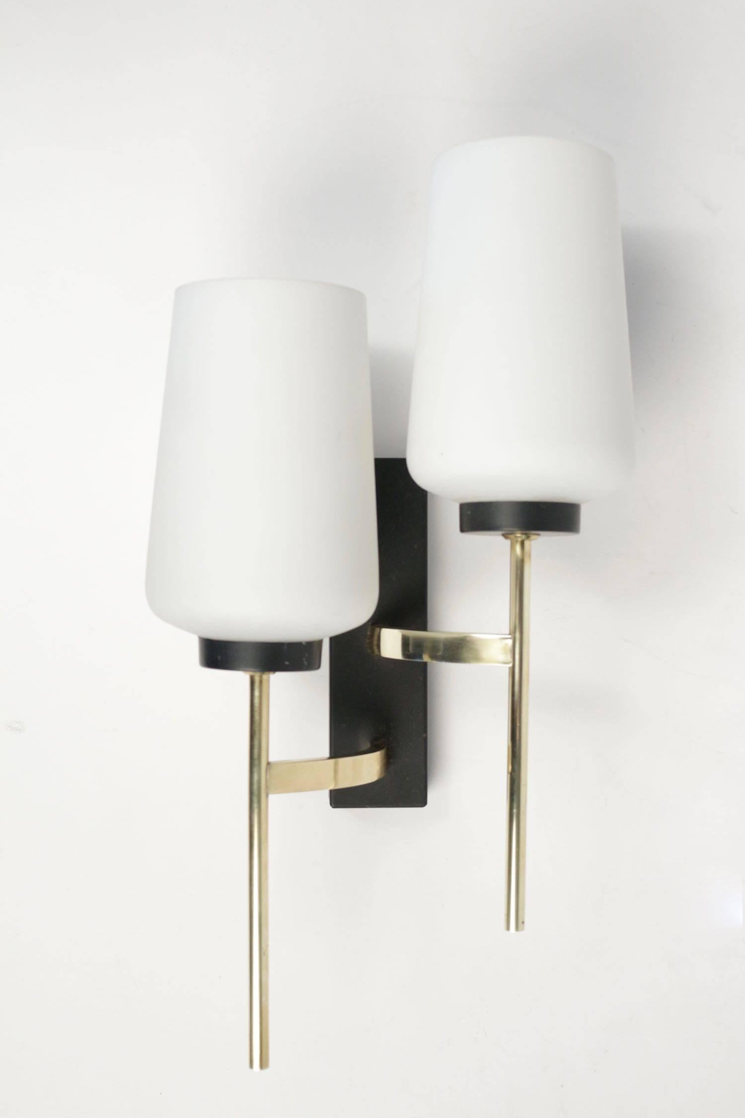 Pair of 1950s asymmetrical sconces by Maison Arlus.
Composed of two gilt brass arms decorated with opaline linked by a gilt brass rod to a black rectangular base.
Two lighted arms per sconce.