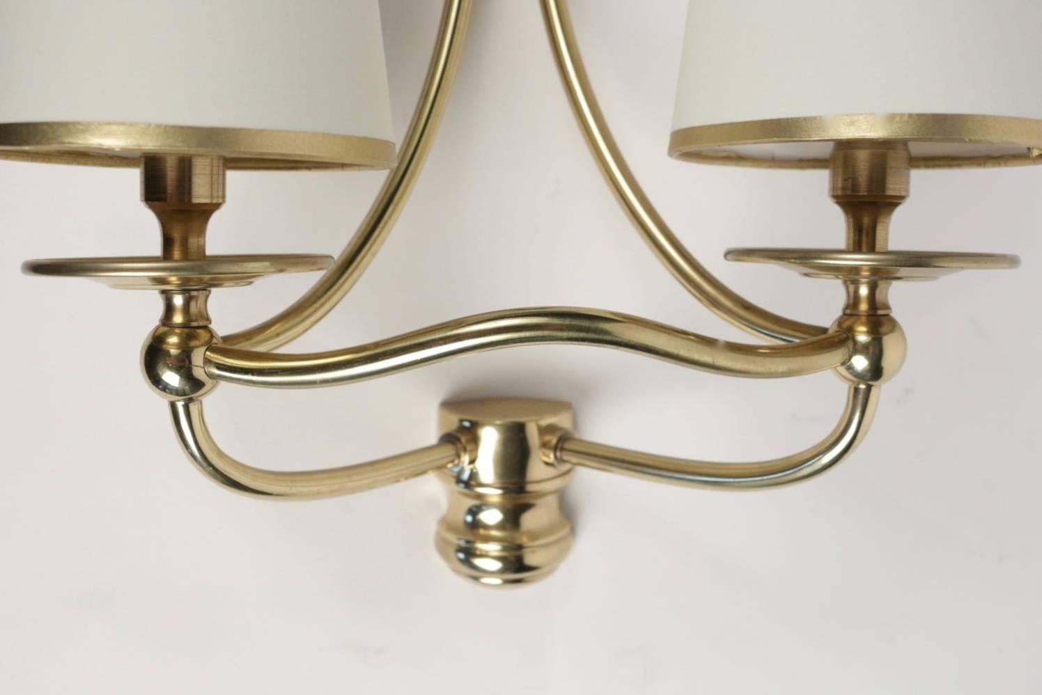 
Set of three sconces in brass, neoclassical, 1960. 
Each sconces consist of two arms assembled with nicely curved brass pipe.
Handmade lampshade in white ivory cotton highlighted with two golden stripes.
 