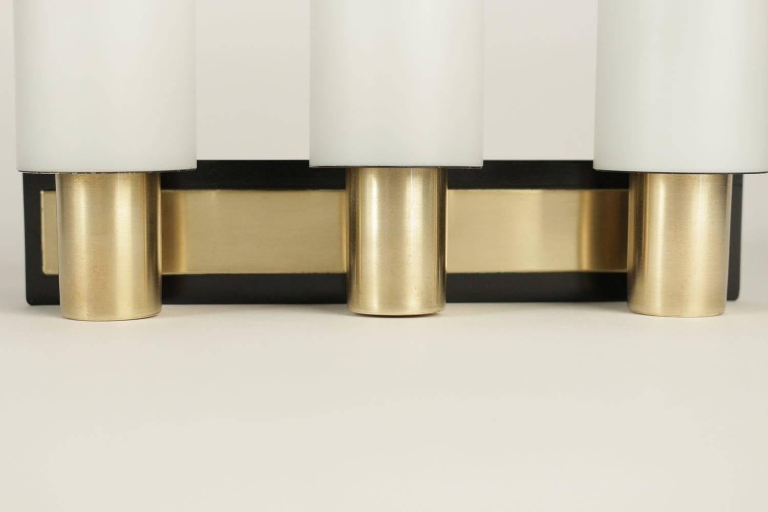 Pair of sconces by Maison Stillovo, 1950.

Each sconce are composed by horizontal brass back plate framed with black lacquer. The back plate supports three cylindrical opaline glass lampshades mounted on cylindrical brass section. Sobre and chic