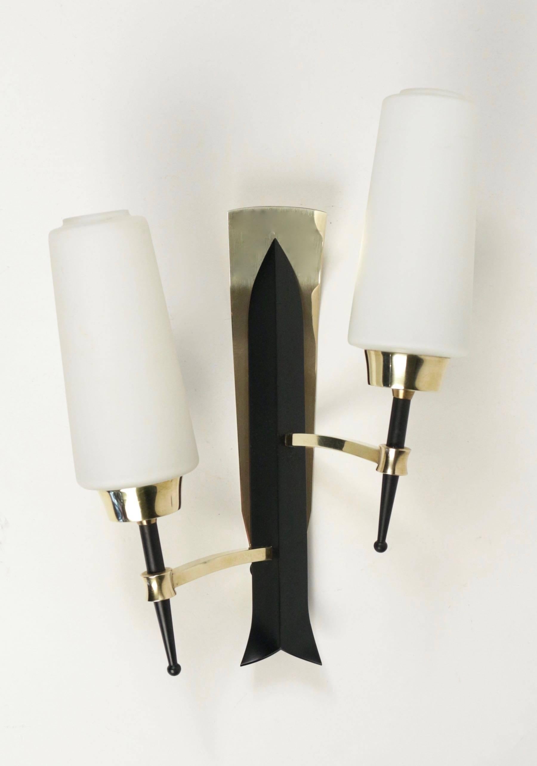 1950 pair of sconces by Maison Lunel.

Backplate made of brass with folded black lacquered stylized arrow.
Two arms in brass support two conical opaline glass lampshades mounted on a black lacquered metal stem ended by a ball.

Two bulbs per