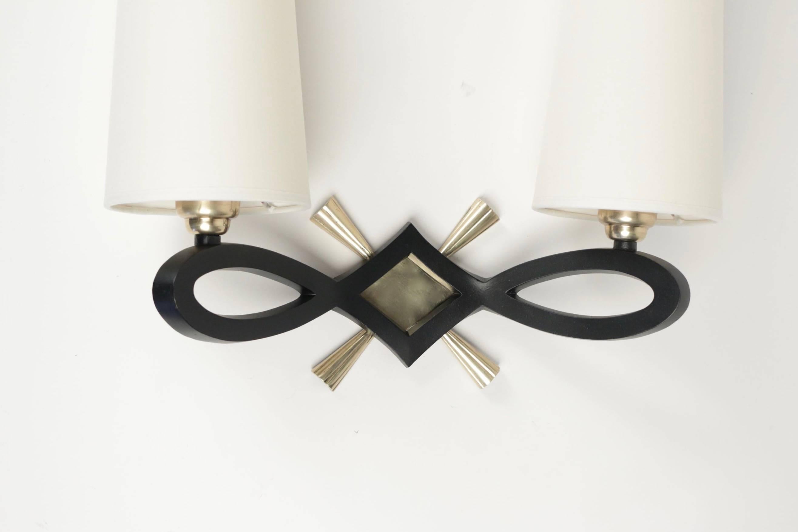 1940 pair of wall lights by Marcel Guillemard.

Each sconce consists in a large black lacquered bronze knot highlighted with a gilded bronze diamond-shaped plate and cross.

Two lighted arms and two white ivory cotton lampshades.

The signature is
