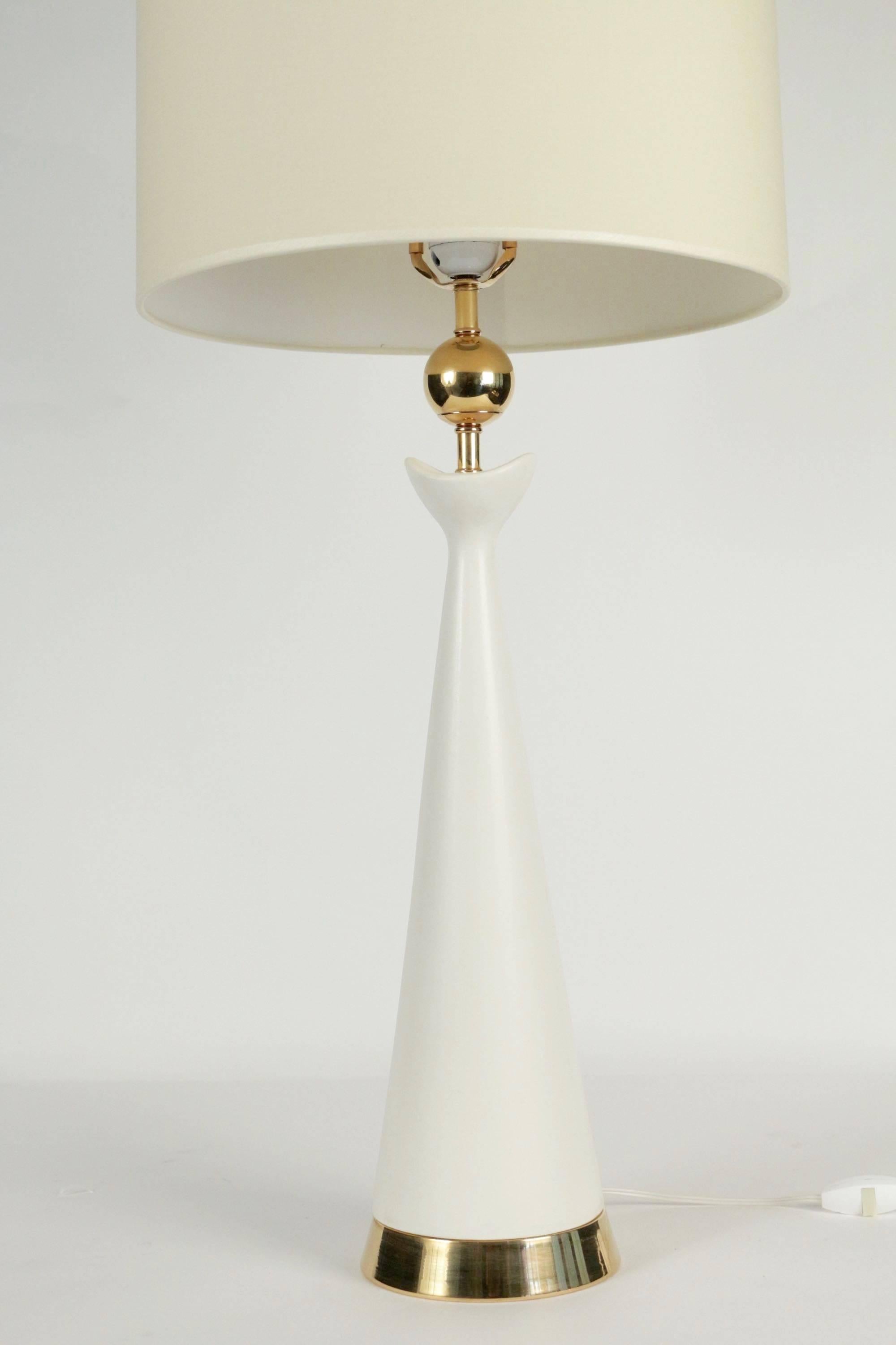 Lamp base made of white enameled ceramic adorned with a brass feet, and at the upper-part with a brass ball. 

Handmade lampshade of off-white cotton. 

One bulb.