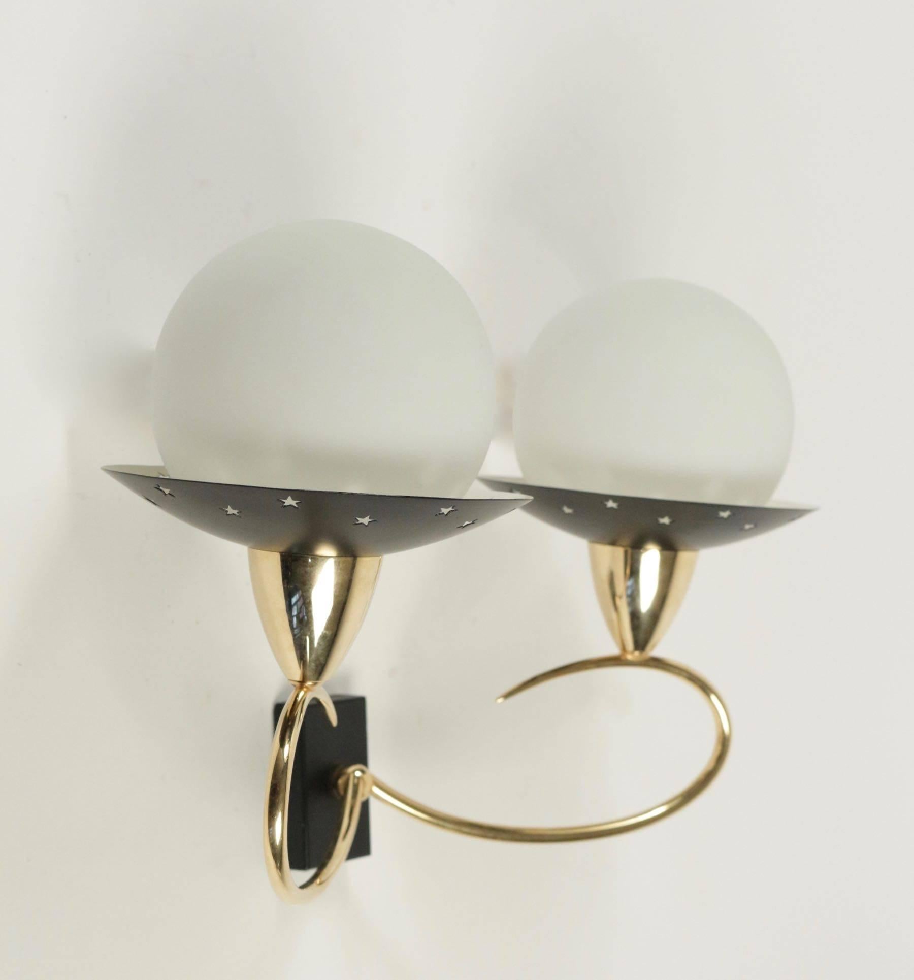 1950s pair of fancy sconces attributed to Stilnovo.

Black lacquered back plate, two curved arms made of brass. 
Two cups adorned with stars. 
Two round white satin glass lampshades. 

Two bulbs per sconces.
 