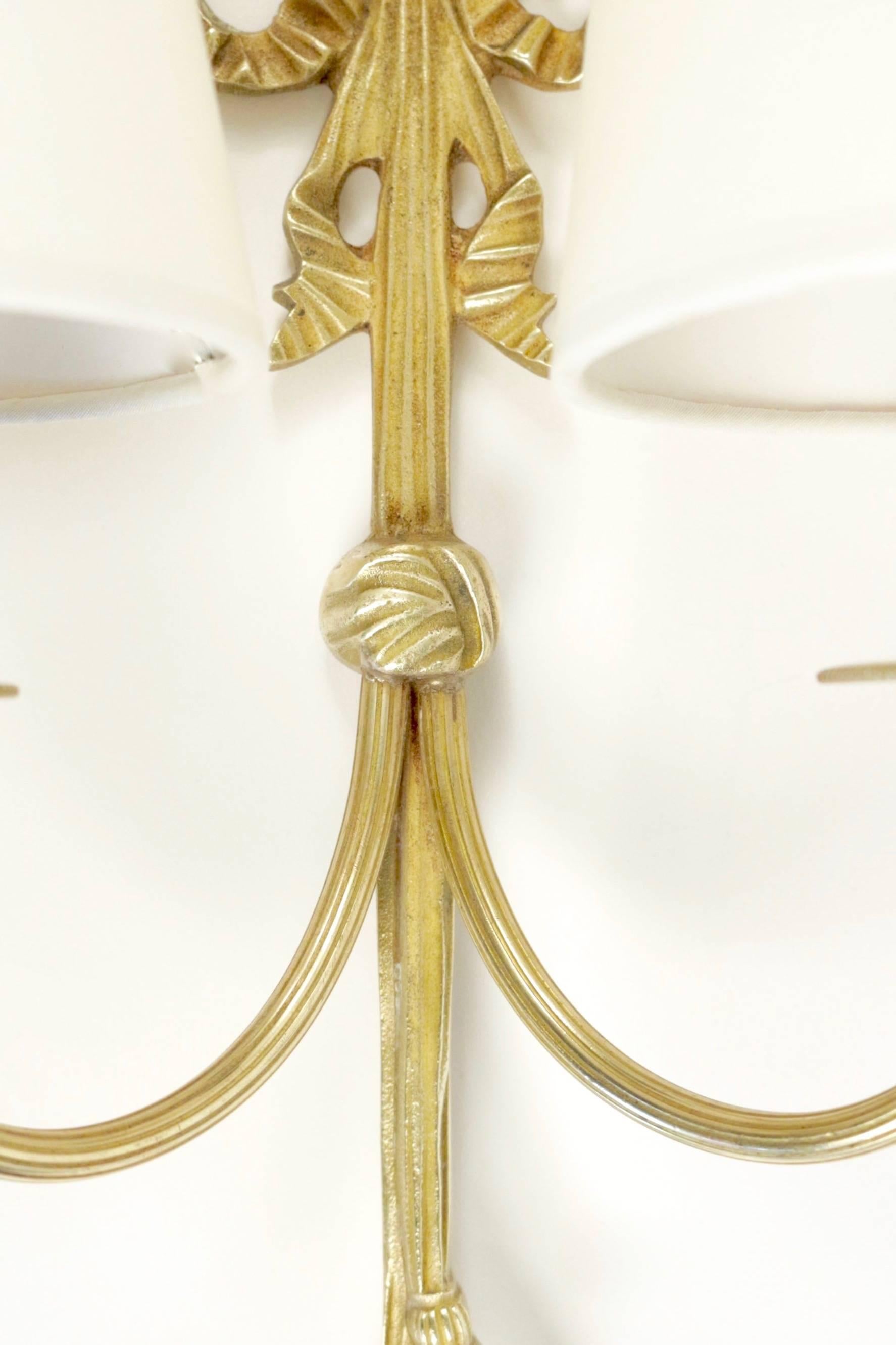 1960s 'Ribbon' bronze pair of sconces Maison Honoré. 

The bronze ribbon back plate supports two lighted arms.
Handmade lampshades made of white ivory cotton granted to the originals.

Two bulbs per sconces.

