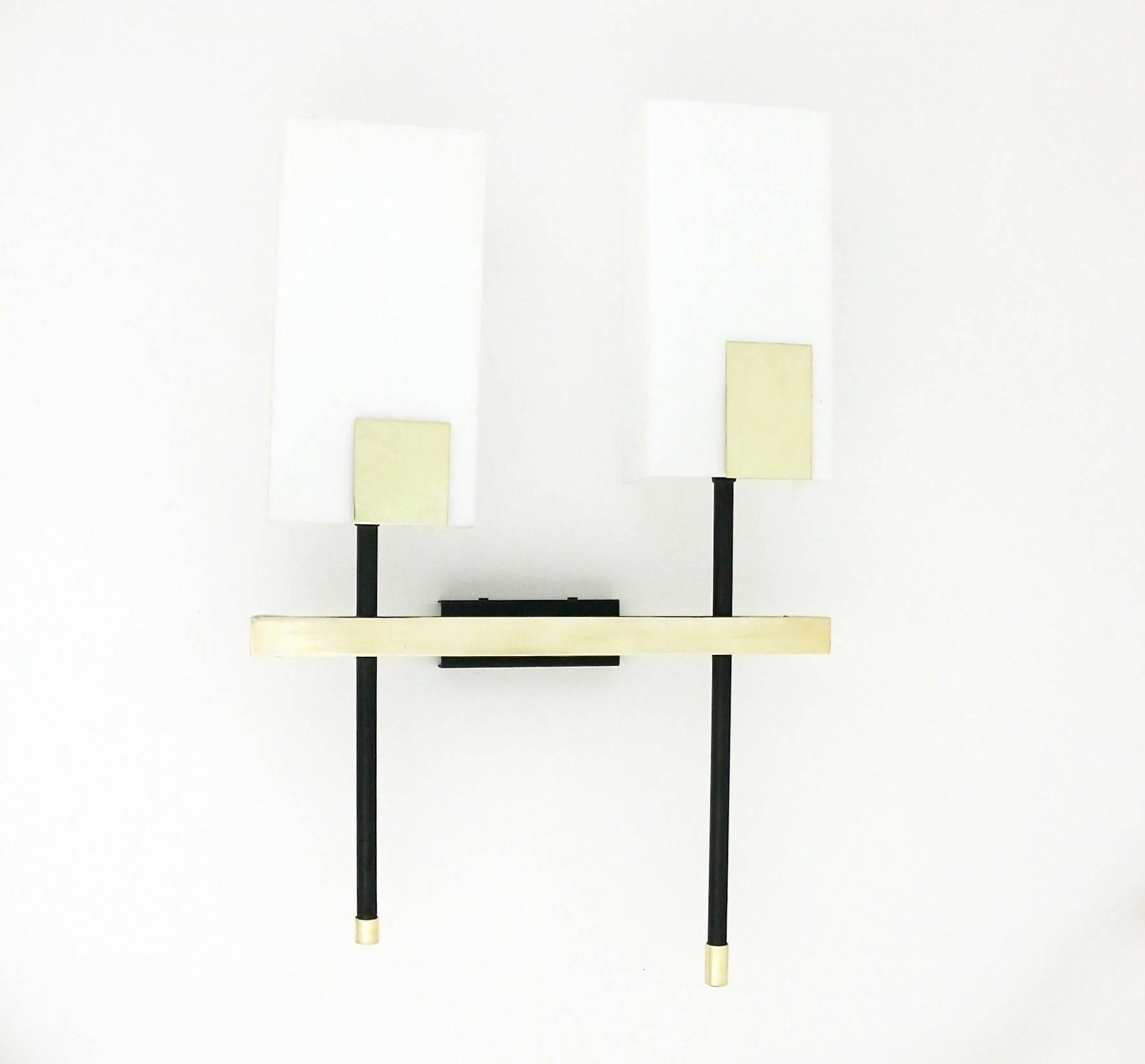 Pair of 1950s asymmetrical sconces by Maison Arlus. 

Composed by two black lacquered stems adorned with rectangular brass plates, mounted on brass crossbar.
Lampshade in white perspex.
 
Two lighted arms per sconce. Wired and in working