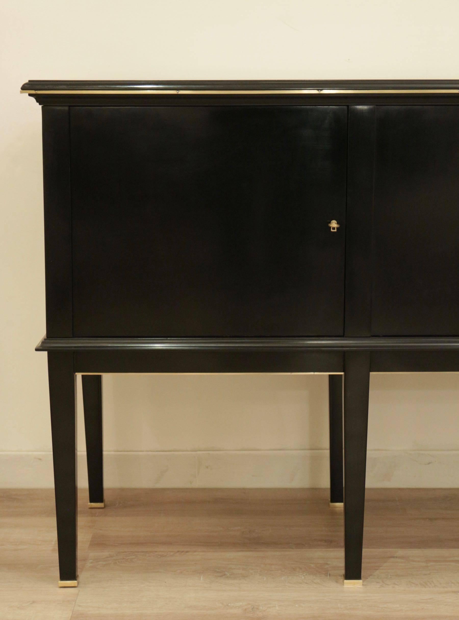 1940s black lacquered sideboard attributed to Maison Jansen

Elegant neoclassical sideboard with four doors soberly adorned with brass details: the eight feet are ended with square section of brass, the doors locks are framed with brass. The