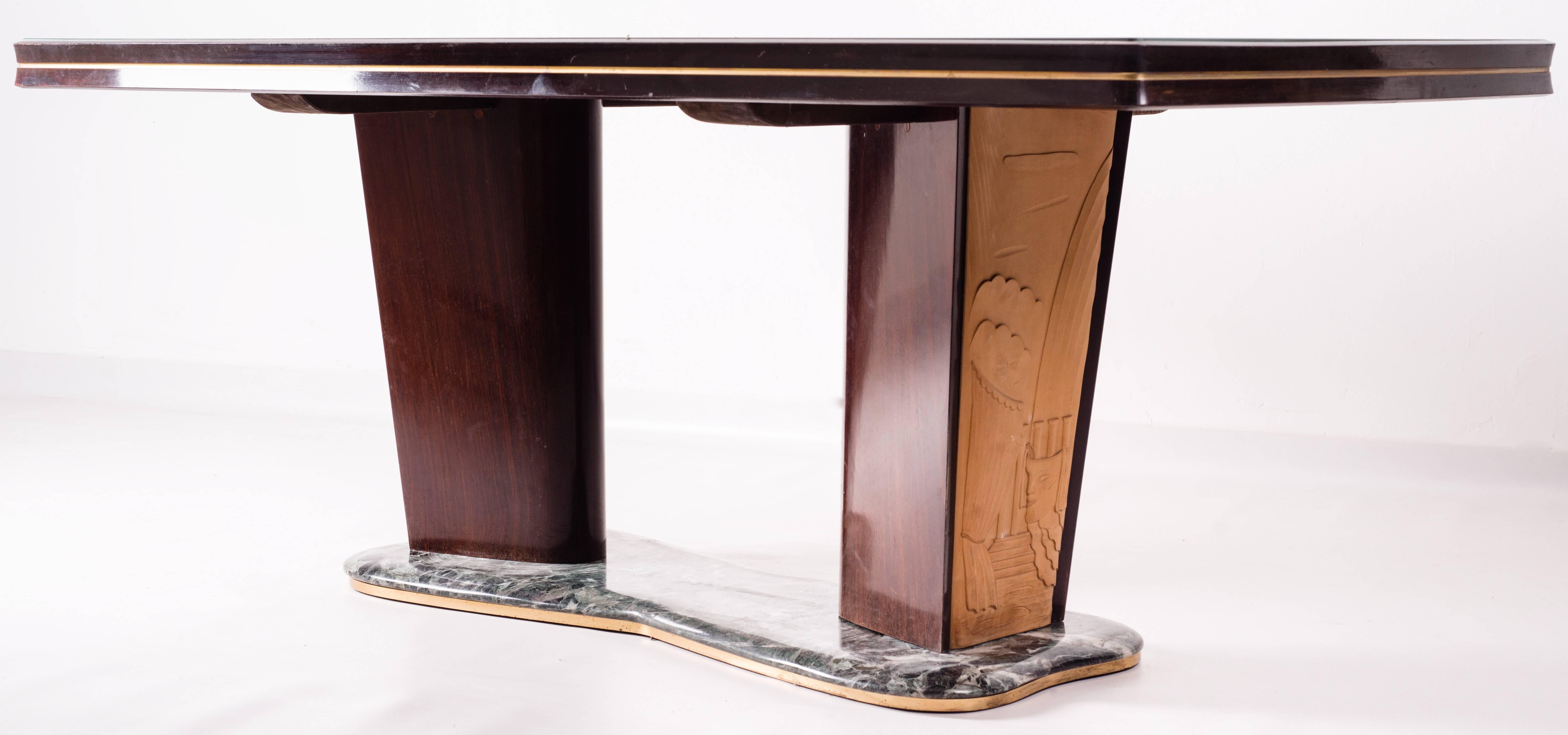 Beautiful table designed by the famous Italian Mid-Century Modern artist Vittorio Dassi, this 1950s dining table has a rectangular glass top supported by two large walnut and maple legs carved with reliefs resting upon a green free-form marble