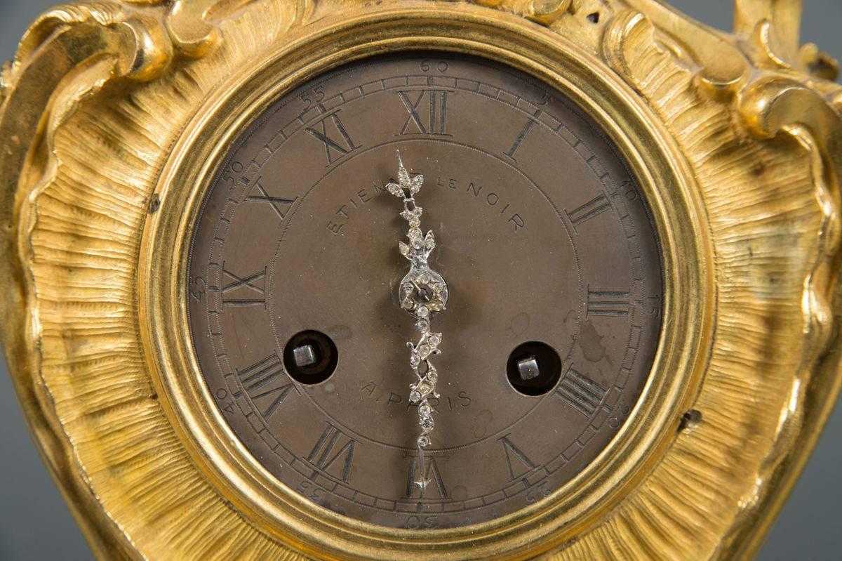 Diese französische Louis-XV-Uhr aus Ormolu-Bronze, die im 18. Jahrhundert von Etienne Le Noir in Paris gefertigt wurde, ist ein Zeugnis exquisiter Handwerkskunst. Das Metallzifferblatt mit einer Mischung aus römischen und arabischen Ziffern trägt