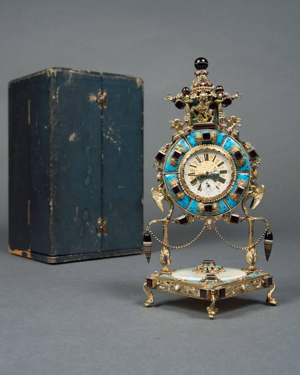 A unusual Swiss made gilt sterling silver, enamel and semi precious stone desk clock with box,

Swiss, circa 1950.

Having various components and intricately crafted using silver, enamel (blue, green, white) mother-of-pearl, tourmaline and