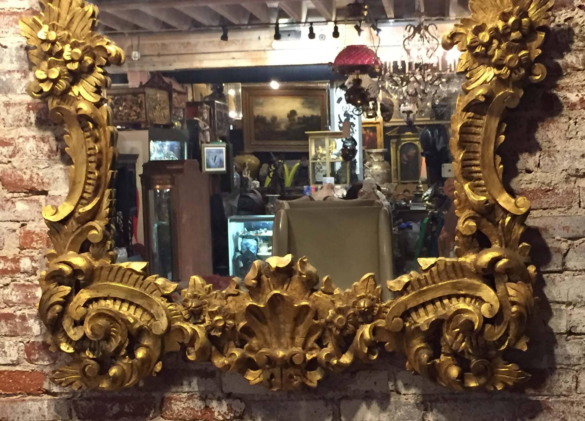 A large and ornate Italian Rococo style gilt wood carved hanging mirror.

Beautifully carved with solid wood and gilded with 24-karat gold.

Provenance: Beverly Hills Estate.

Measures: Height 83