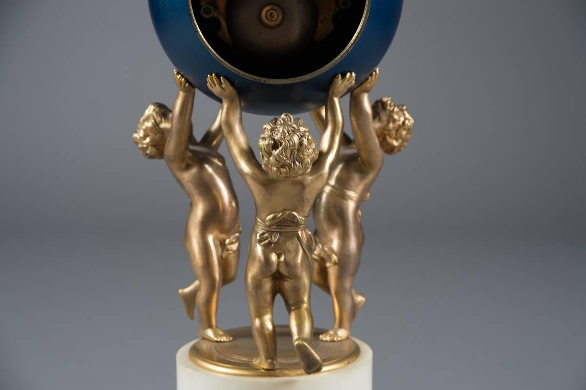 A fine French Napoleon III gilt bronze and white marble mantel clock 

France, circa 1855

Having three putti raising a globular enameled clock case with Roman numerals. Standing on a white marble base with a gilt bronze garland surround.