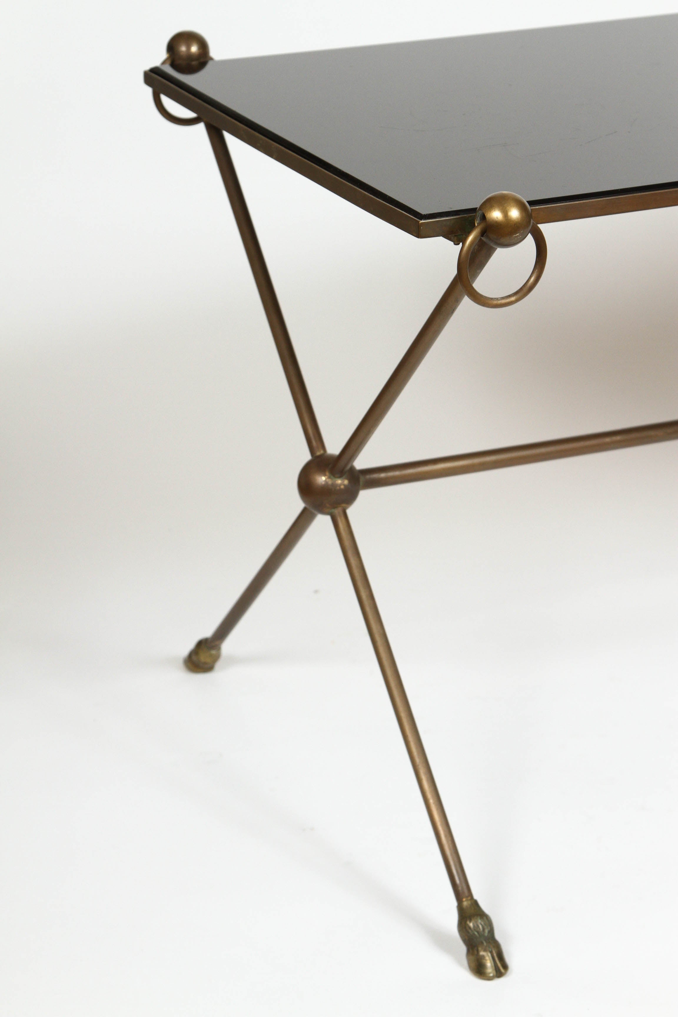 Vintage Maison Baguès brass cocktail table with black opaline glass top resting on an X-base. Features bronze and brass stressed rings and spheres at the corners, legs stand on hooves. Made in France, circa 1950.