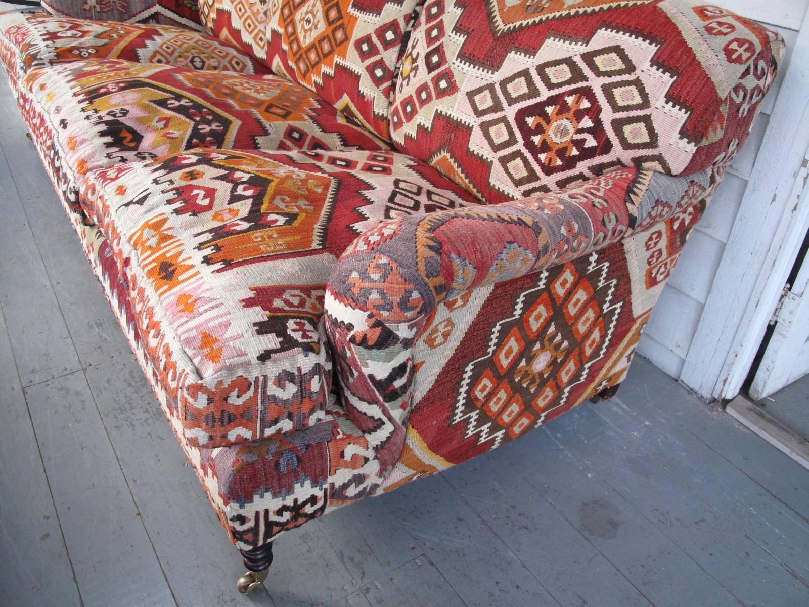 Down filled. Upholstered in vibrant wool Kilim. Three turned front legs on casters. Made in England by Fine furniture maker George Smith.